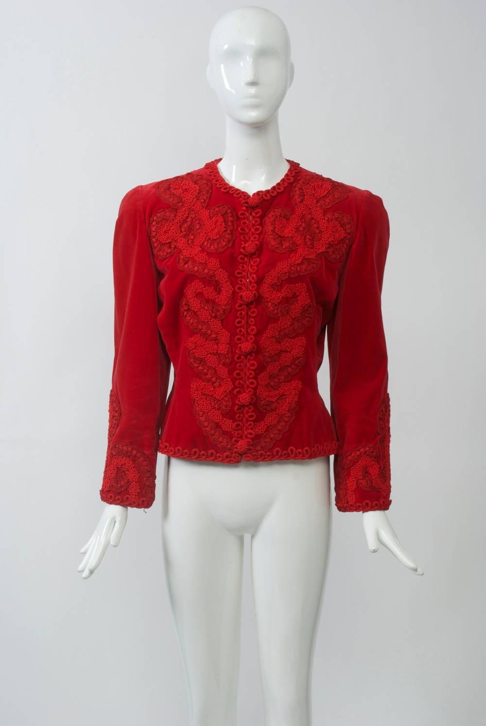Red velvet jacket with elaborate soutache embroidery trim down front, across back yoke and at wrists. Fitted body, collarless neckline, front loop closures with knotted buttons. Hook and eye clasps underneath may have been added. Padded shoulders.