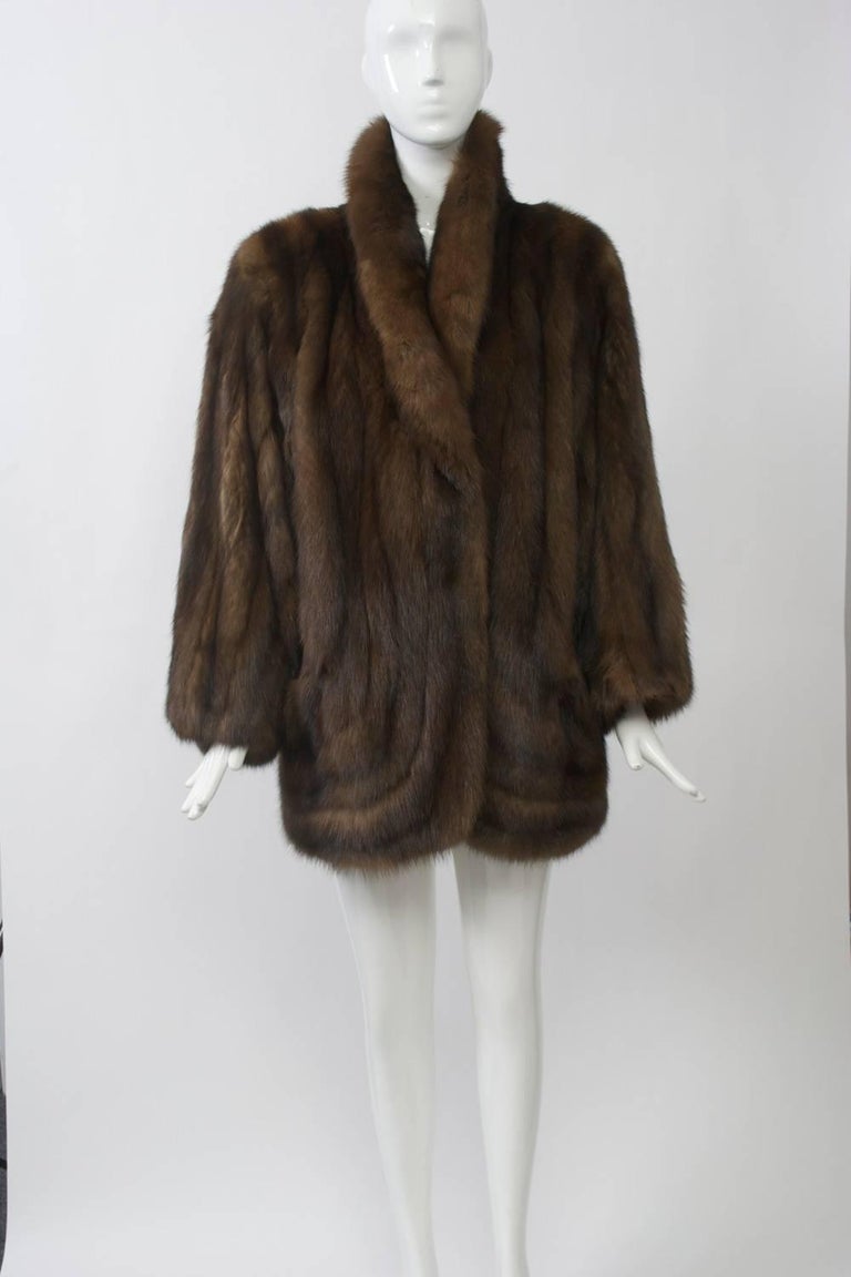 Luxe sable jacket features a shawl collar and curved skins at bottom front with small slash pockets. Dolman sleeves and loose fit allow for ease of wear and casual look. Nice medium brown skins. Mid-thigh length. Approximate size Medium.