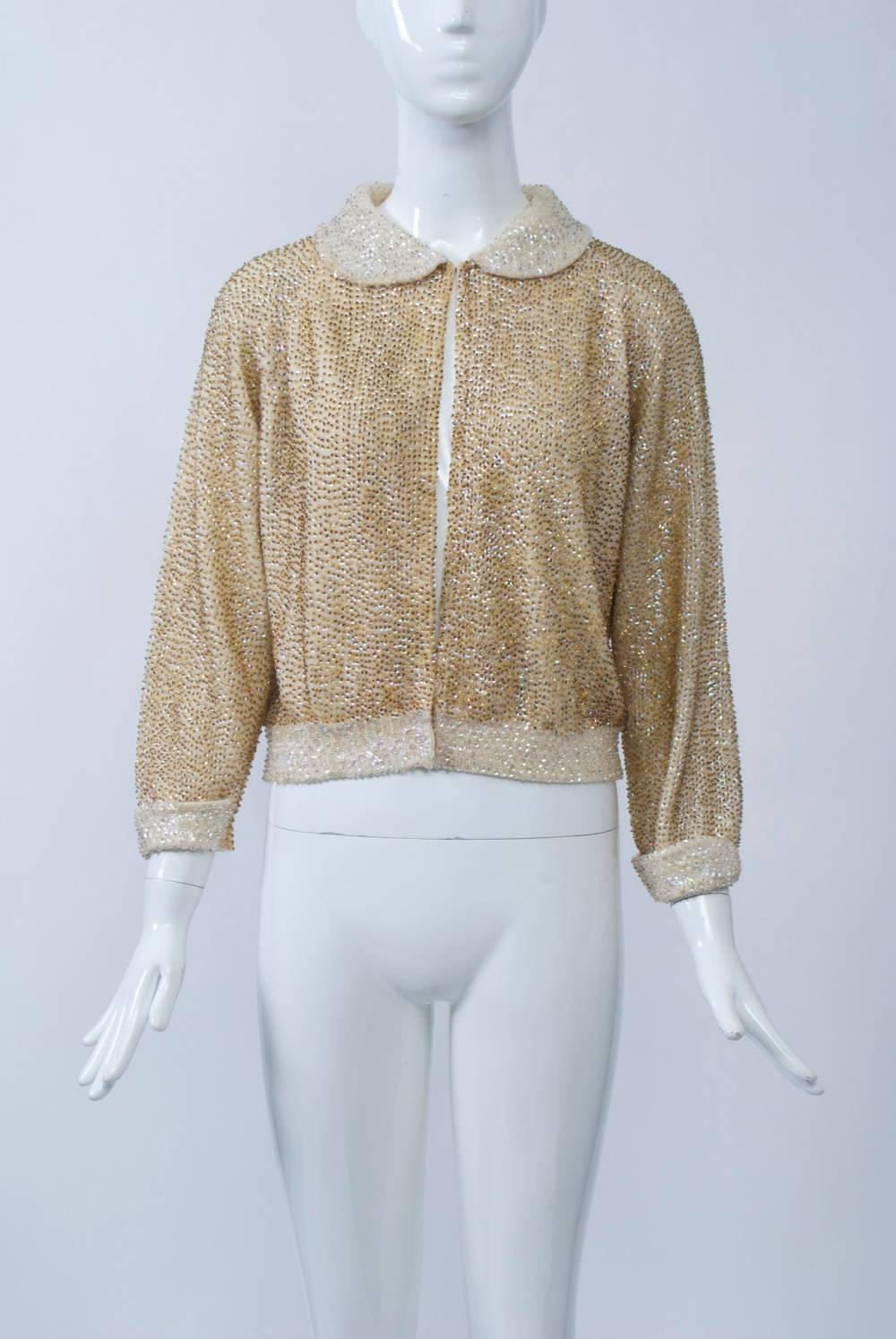 Allover sequined and beaded cardigan on an off-white knitted ground, the body with iridescent sequins and small gold beads, the collar, hem and wrists with iridescent sequins and clear beads. Peter pan collar and turned-back cuffs. Hook-and-eye