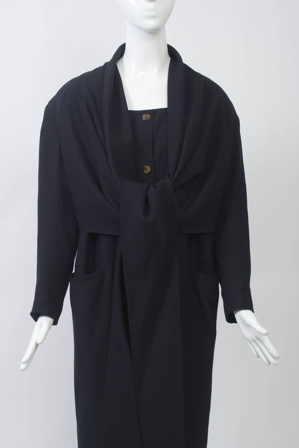 Button-down dress in dark navy gabardine that is distinguished by an attached cape with long, tapered ends that wraps crosswise in front and ties behind the back; it can also be worn in different configurations as shown. The dress features a high,
