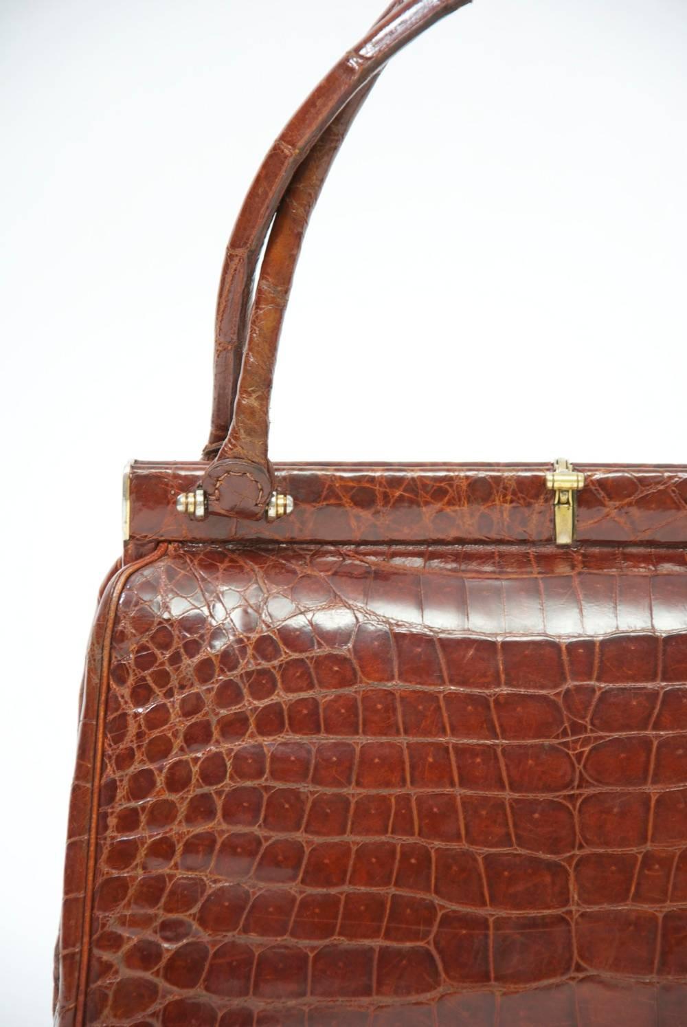 Classic 1960s handbag in cognac crocodile featuring a double handle and a discreet brass clasp. The interior, in matching leather, has open side compartments with snaps, and an additional zippered compartment on one side.