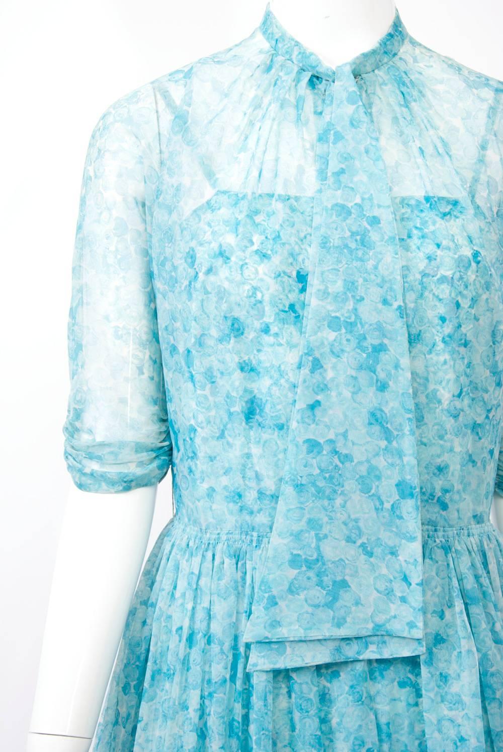 Early Leslie Fay ensemble in matching aqua prints, the shirt-style overdress or coat in sheer fabric featuring three-quarter shirred sleeves, buttons to the waist, a full skirt, and a self tie at the neck. Underneath is a sundress, possibly acetate,