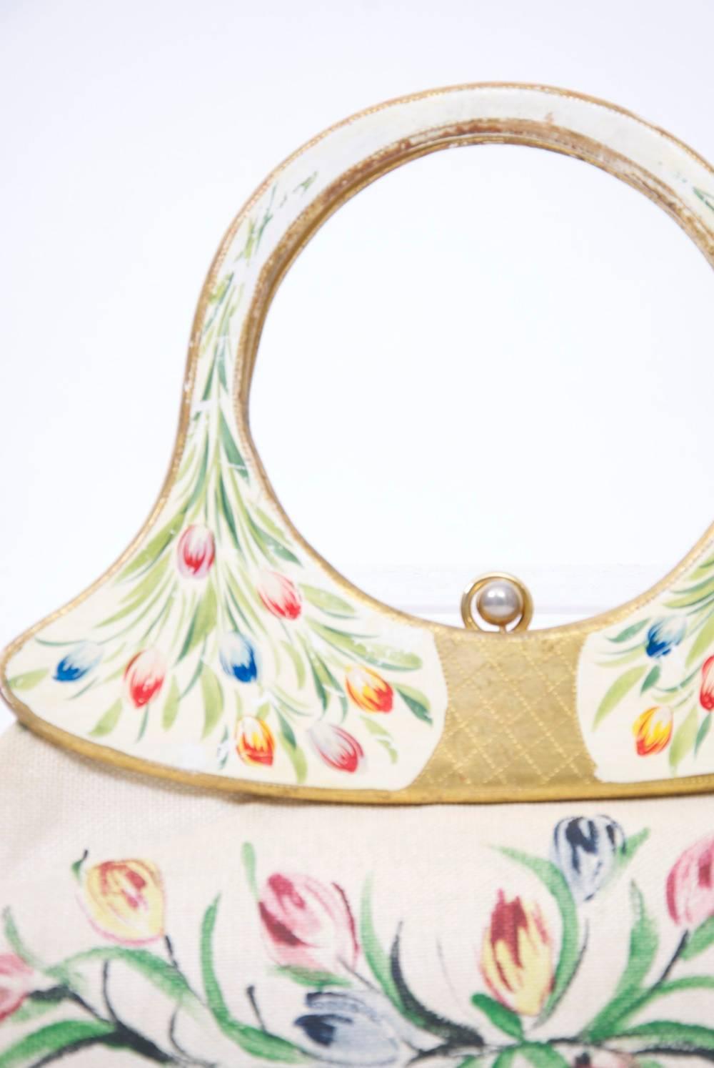 Unique, ivory woven summer bag hand painted with multicolored tulips across the wide body front and back, as well as on the double wooden loop handles, which are painted in gold, except for the white ground on which the tulips appear. Ball clasp.