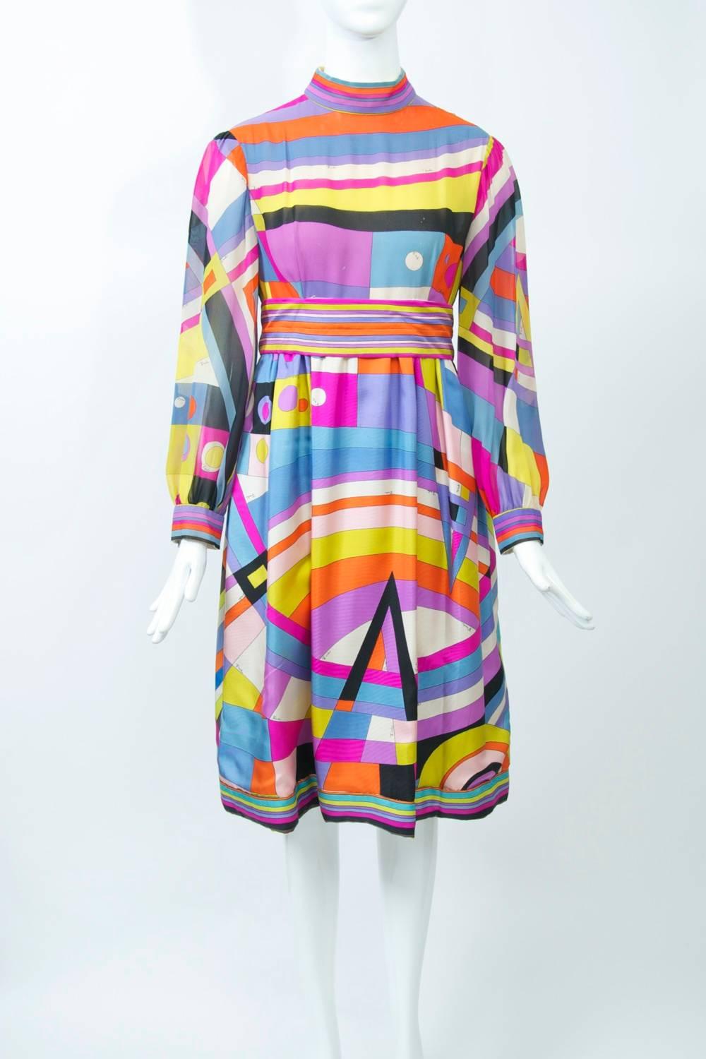 Pucci vivid geometric print dress, the bodice of silk chiffon, the skirt of regular silk in blues, purples, fuchsia, yellow, orange, white and black. The empire bodice features a mock turtleneck and long full sleeves with border at the snapped cuffs
