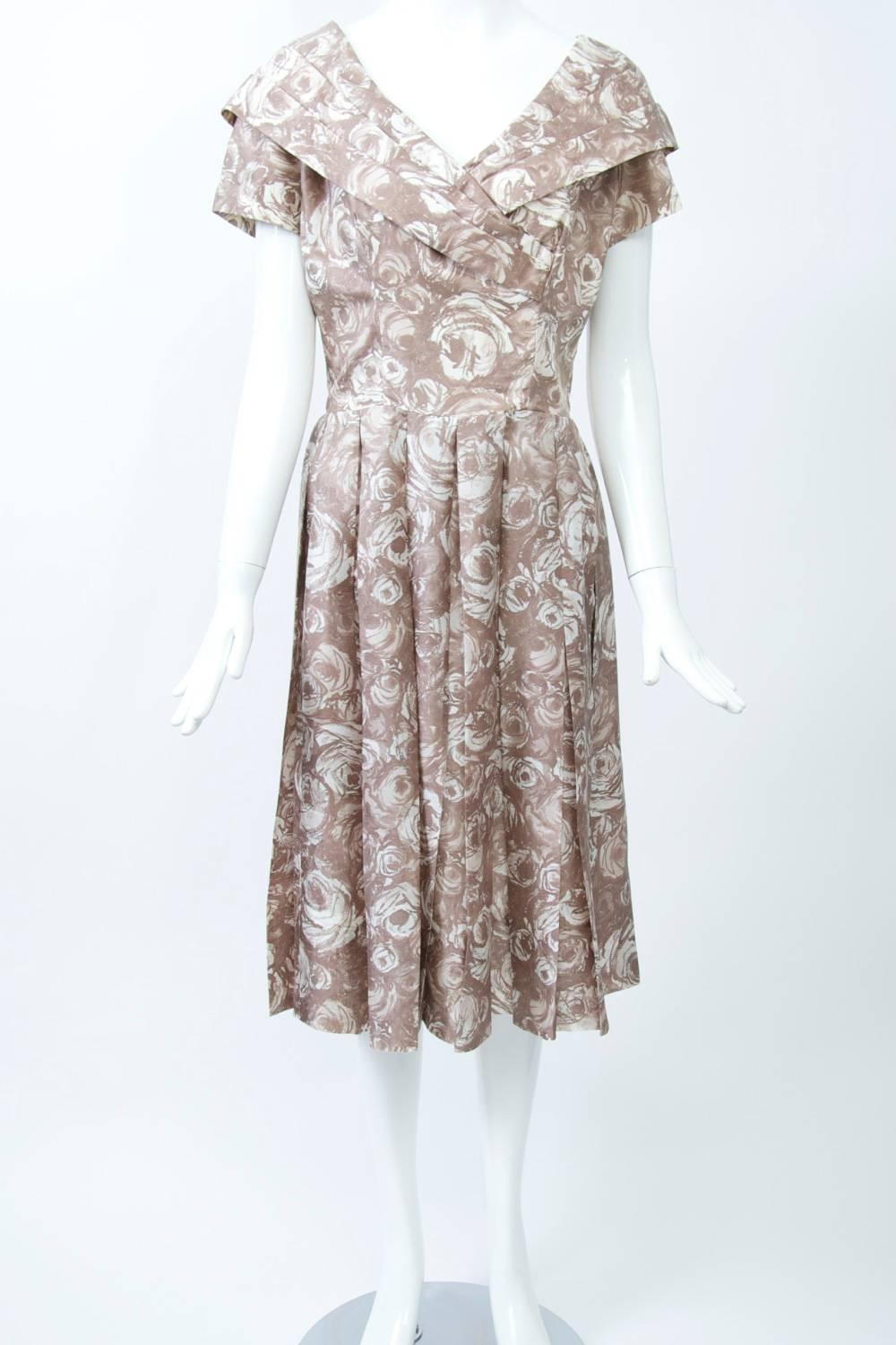 Suzy Perette 1950s-'60s silk dress composed of a tan and white abstract floral print. The dress features a surplice V-neckline with wide and pleated shawl collar, short sleeves, and fitted bodice; below the seamed waistline is a soft skirt with wide