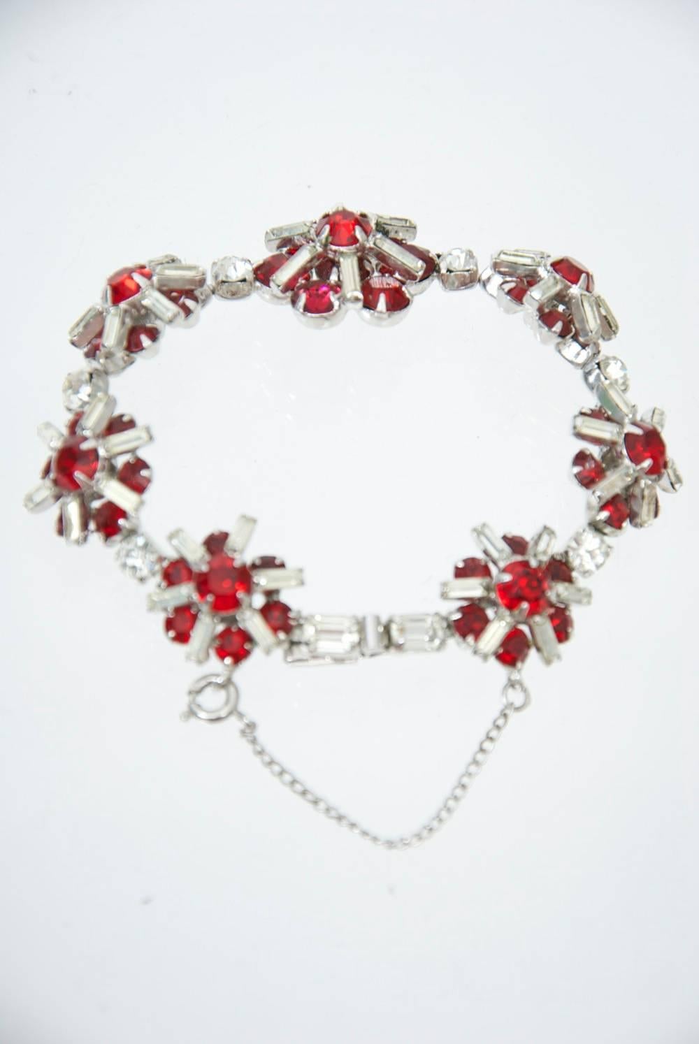 Bracelet fantaisie vintage Kramer composé de fleurons en cristal rubis et strass, un plus grand au centre, reliés par un seul strass entre chaque fleuron. Chaîne de sécurité.