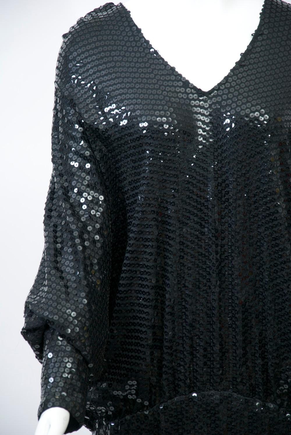 1980s black sequin blouson dress featuring a V neck, a narrow skirt with side slit, and deep cuffs terminating the long, loose sleeves. Elastic hip. Pulls over the head. Unlabeled. Flexible sizing 6-10.