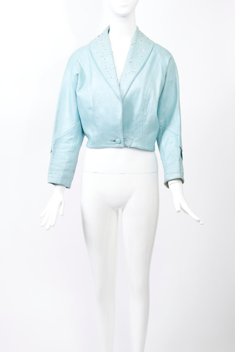 1950s waist-length jacket in pearlized blue leather, its shawl collar studded with pearls and rhinestones, as is a strip below the elbow on the raglan sleeves. Single button at the waist. Curved, longer back with slight slits at sides.
