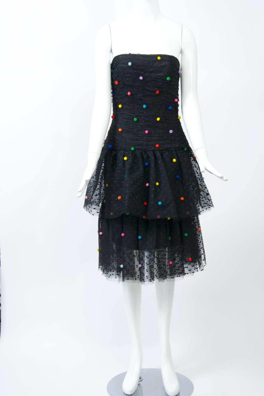 What fun! Victor Costa evening dress in dotted black net, the ruched bodice and tiered skirt decorated with multicolored mini pompoms. Long fitted torso, back zipper, lined with narrow, short underskirt. Approximate contemporary size 4-6.