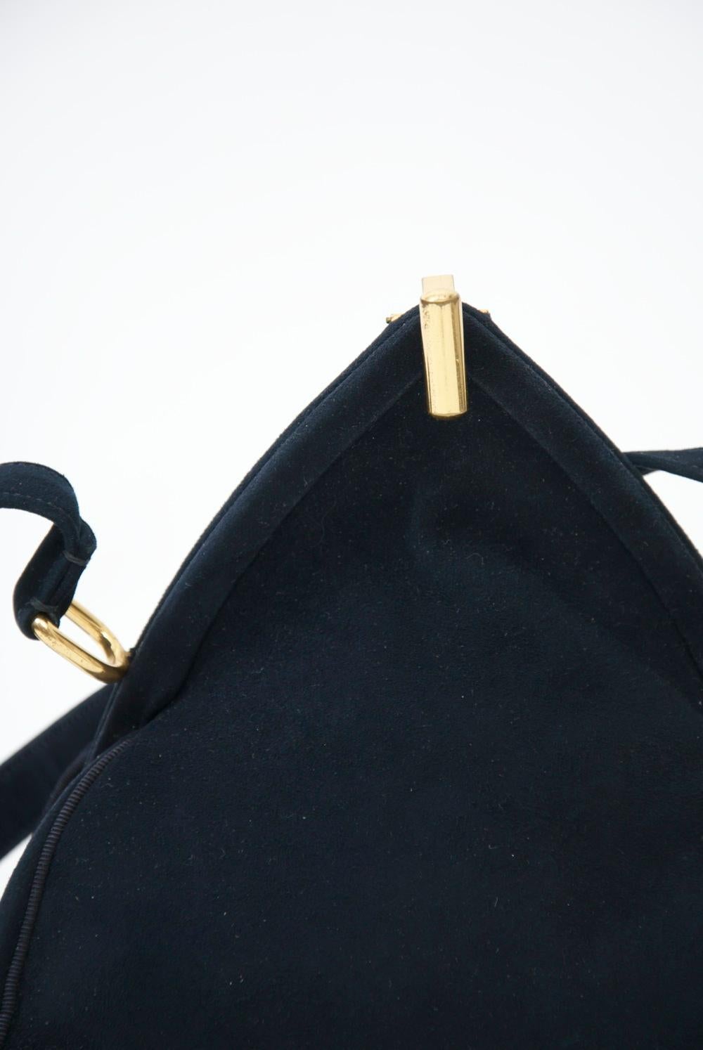 Vintage navy suede handbag in an unusual triangular shape and nice hardware, including the flip-up clasp. A single strap is attached to matching metal elements mounted at right angles to the suede-wrapped frame. Interior is navy satin with side