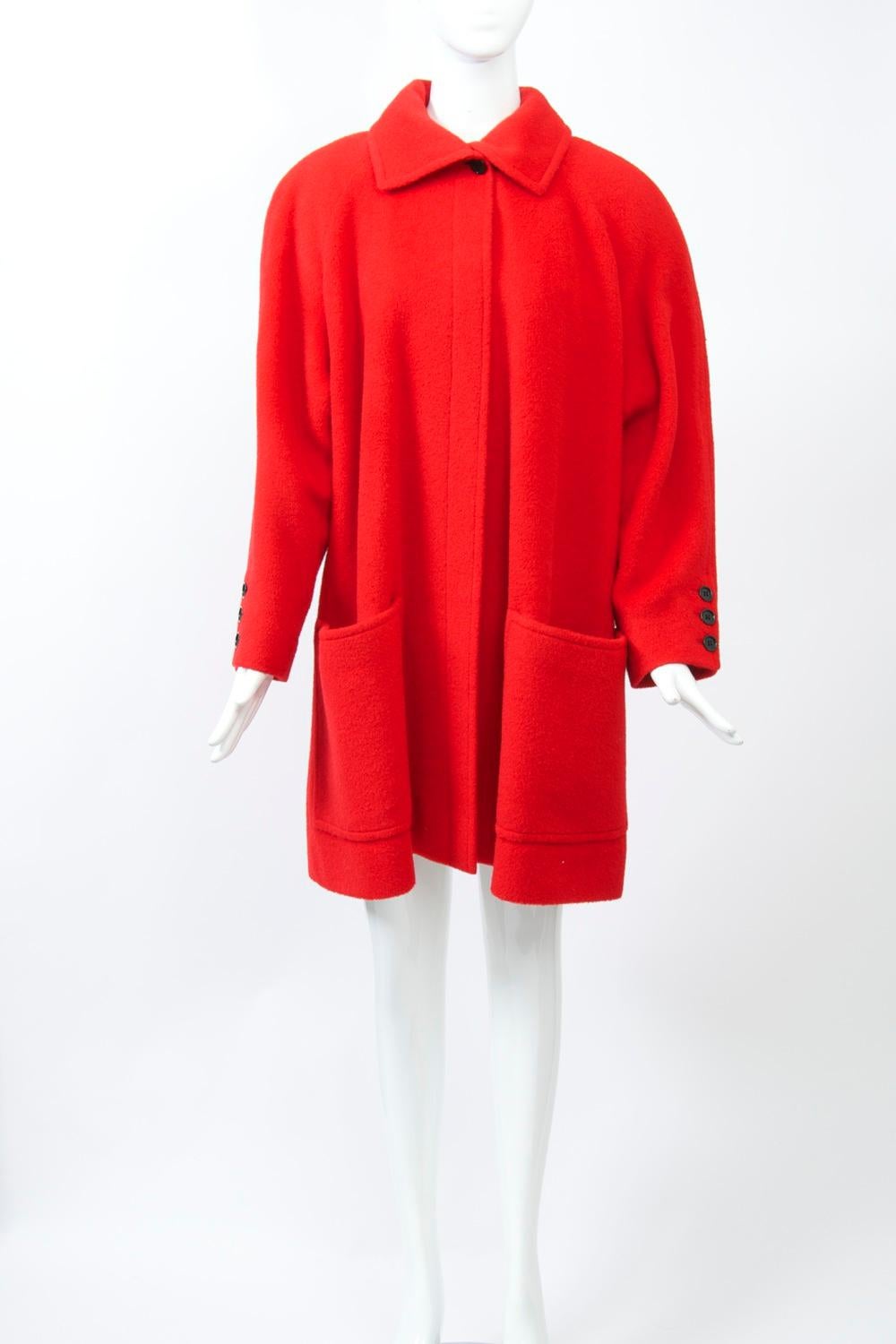 Plush red wool lends this Tiktiner coat its eye-catching quality. The short coat, c.1980s, features a loose cut with deep raglan sleeves, two large patch pockets, a swing back, and a single black button at the neck collar. Three black buttons