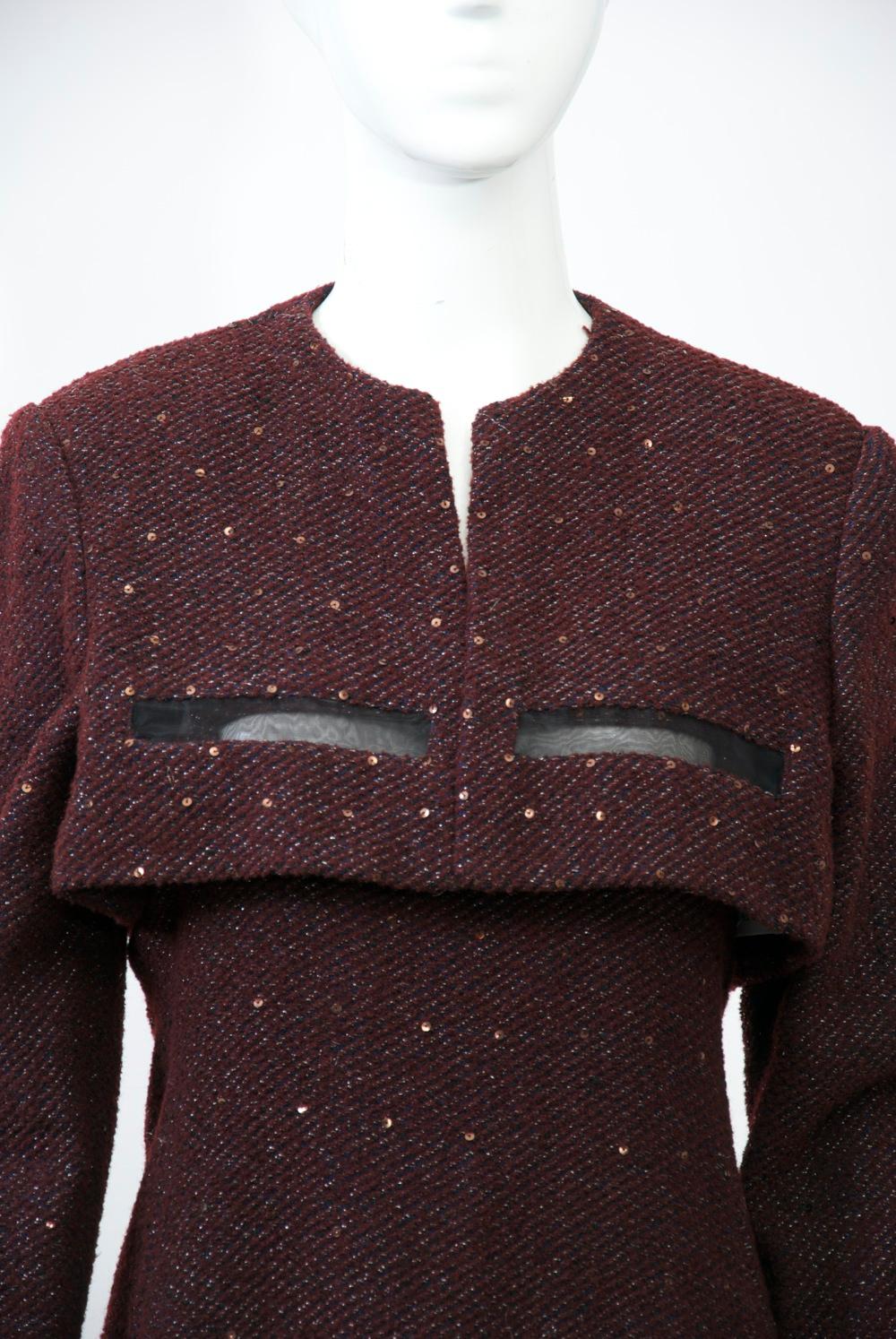 Chic Geoffrey Beene ensemble consisting of a slip dress and a bolero jacket crafted of a lightweight burgundy knit shot through with silver threads and accented with subtle sequins throughout. Each piece features overlapping rectangular “windows” of