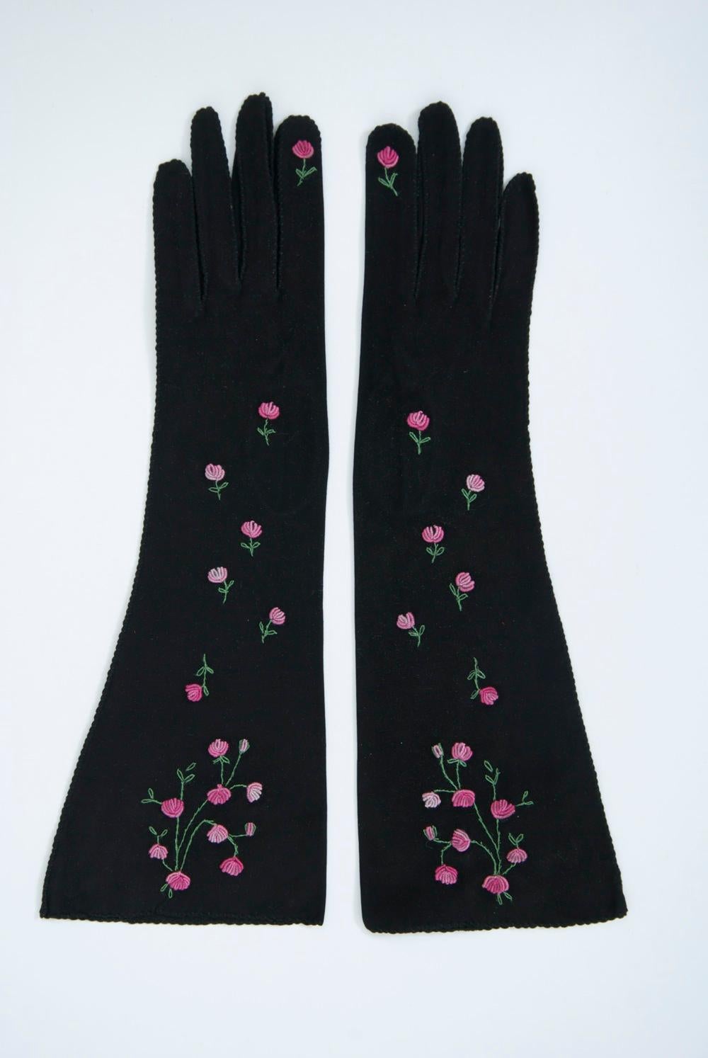Mid-length gloves in black suede adorned with ombre pink embroidered flowers on the top and single flowers on the second and pinkie fingers. 1950s-'60s. Approximate size 7.