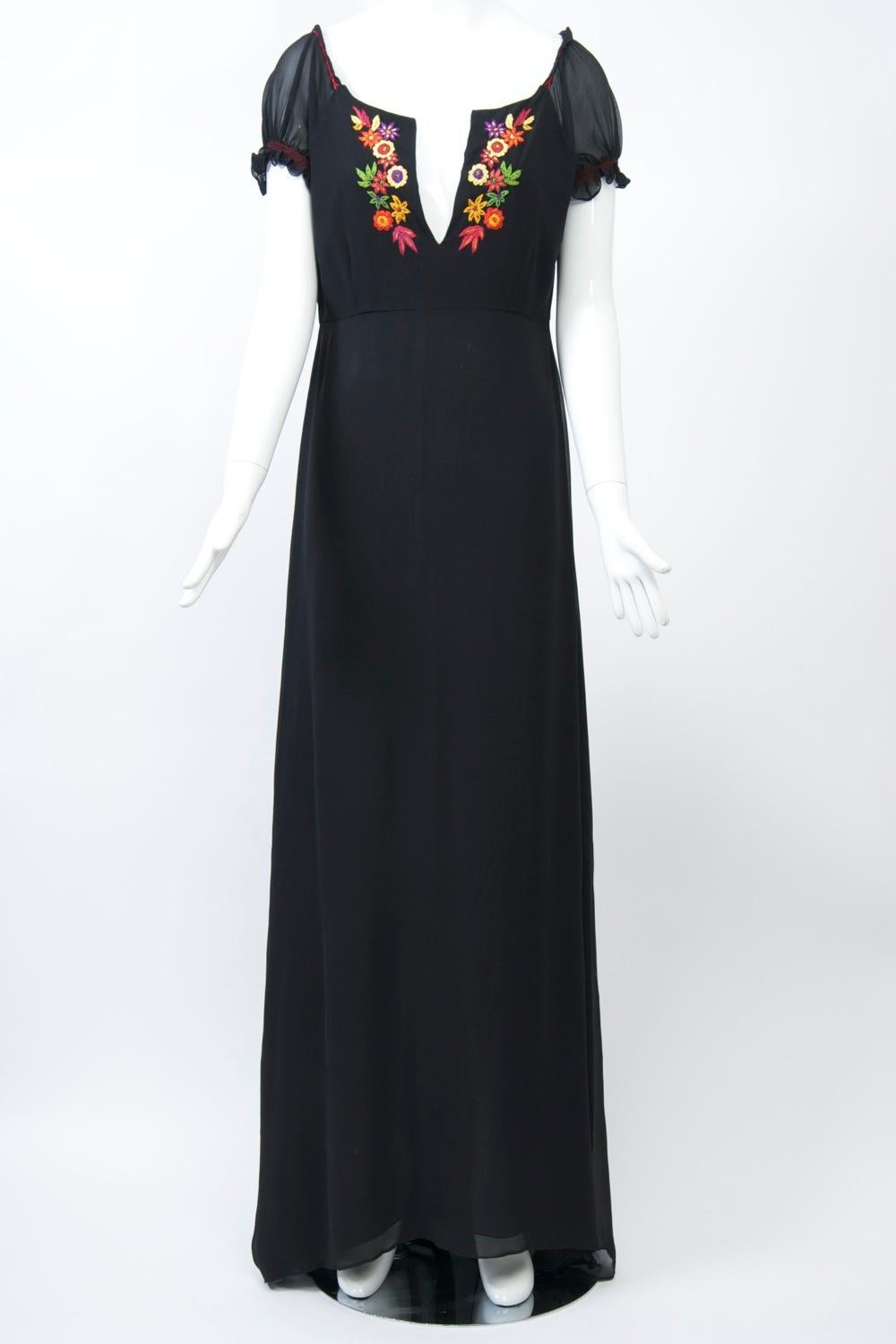 Long dress in black silk featuring ethnic multi-colored embroidery along the low-slit, scoop neckline. The sheer cap sleeves and shoulders are trimmed with red stitching. High waistline. Approximate size M.