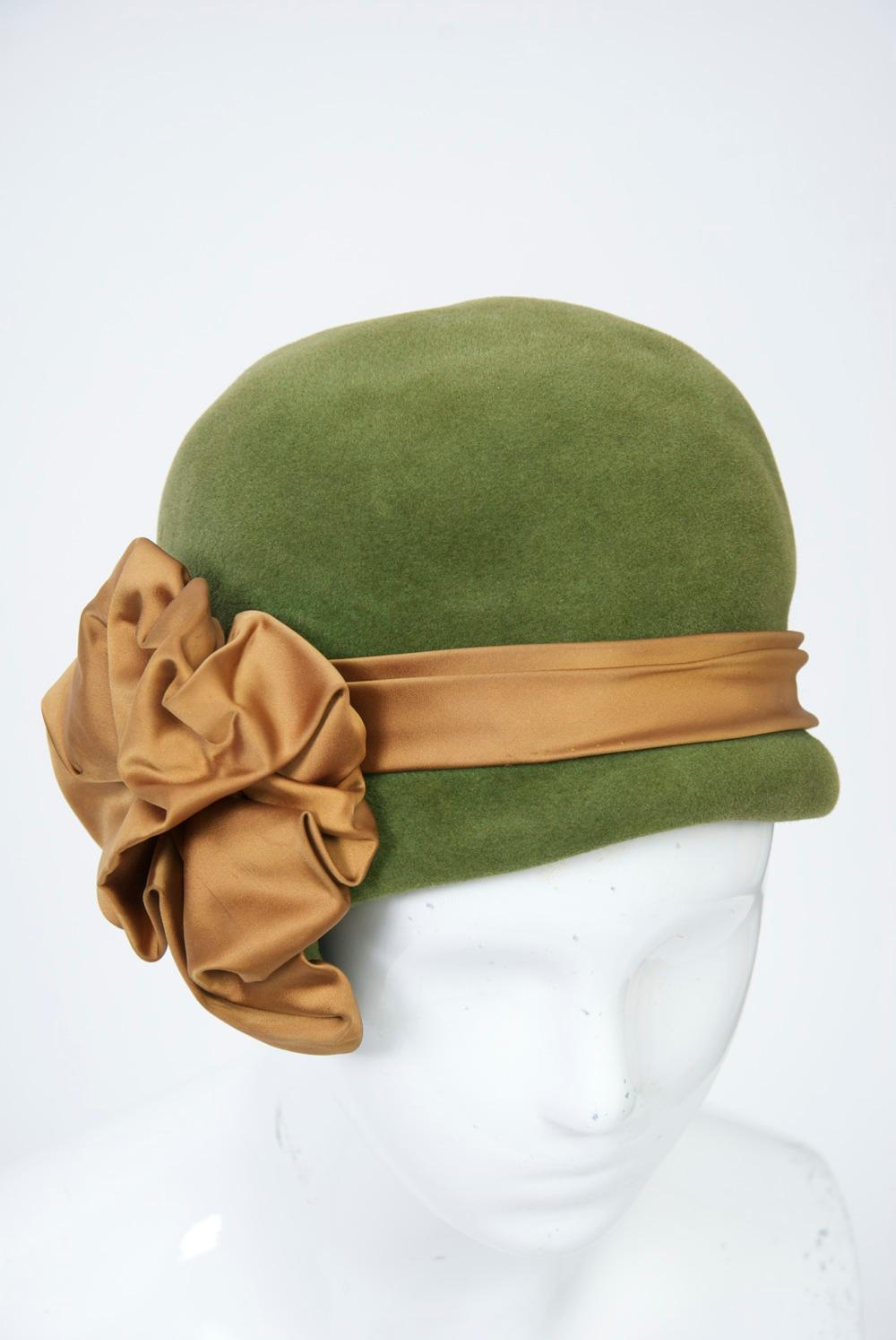 Cloche-style hat in olivey shade of green felt ornamented with a cocoa satin band and large bow on the side. American adaptation of a Pierre Balmain design.