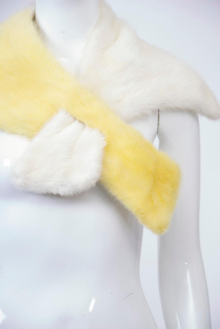 An unusual mink accent scarf of asymmetric design, half in white mink, the other half in yellow mink. The yellow side features a slit through which the white end passes and stays in place.