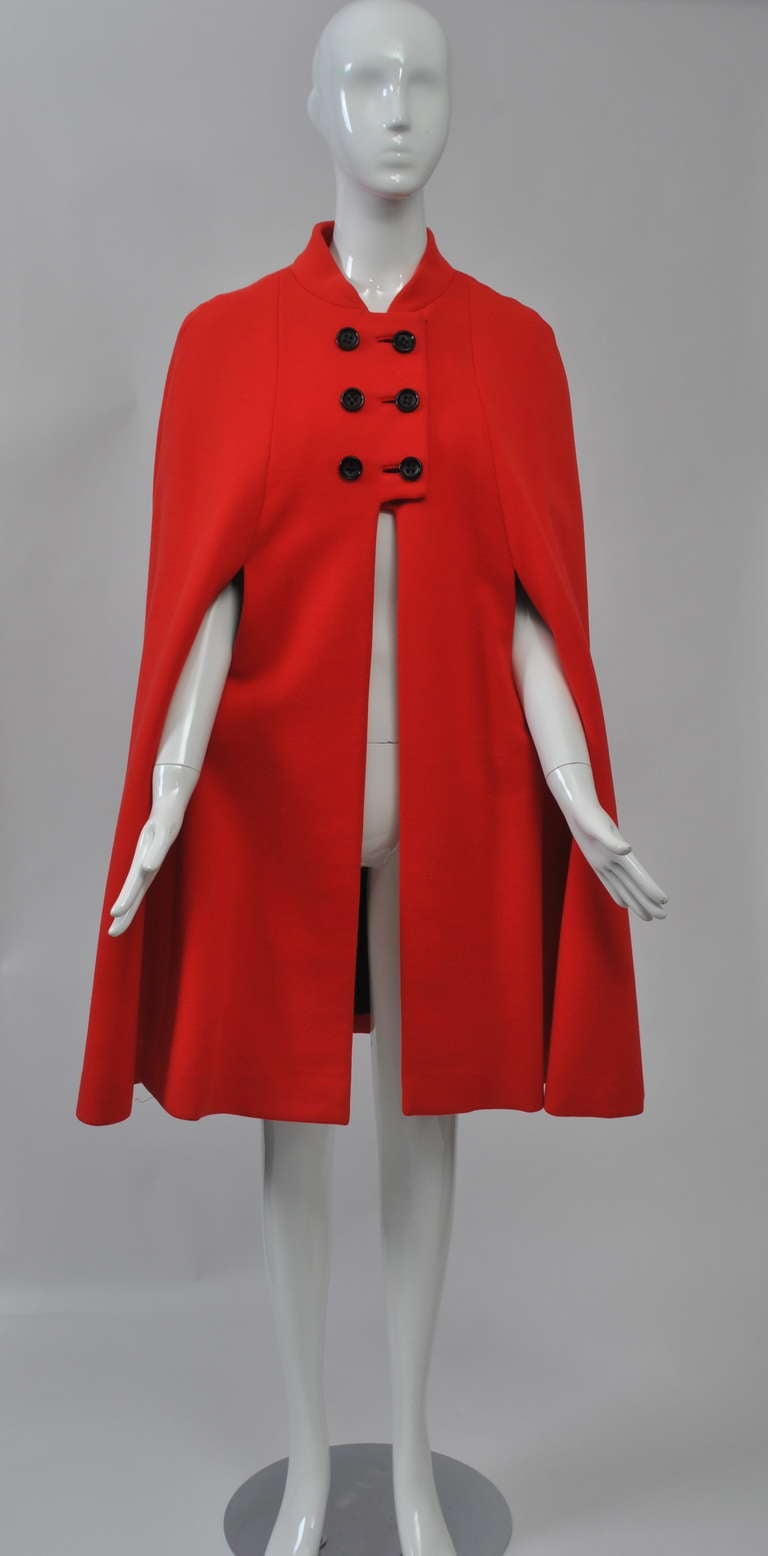 Bright red cape in wool knit with arm slits, double breasted detailing and mandarin collar. Black crepe lining. Perfect complement to black. Small size - 32