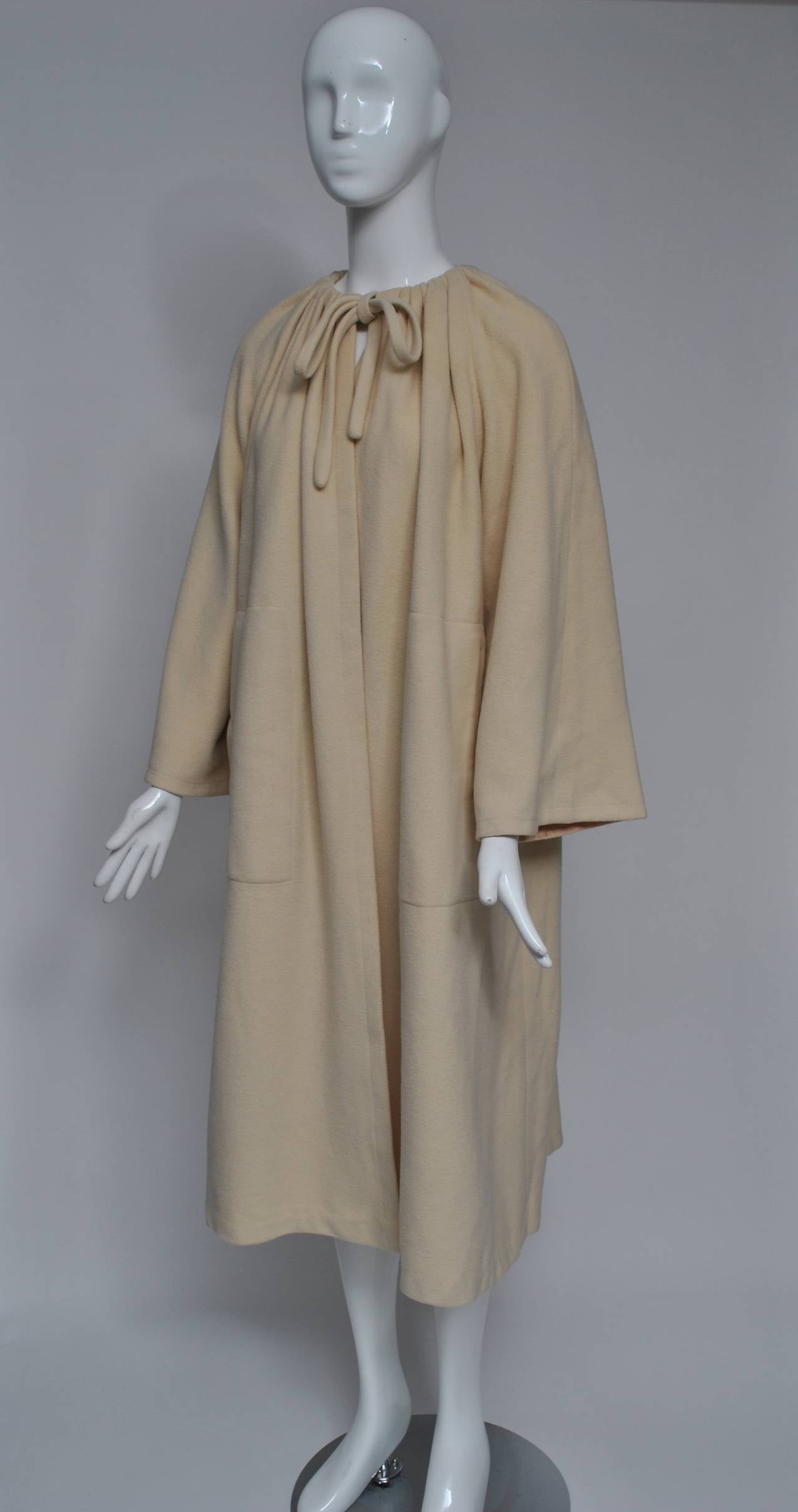 A classic, timeless design from the 1970s, this ivory beige cashmere coat features a drawstring neckline with tie, raglan sleeves, and bound, slash pockets. By Bill Haire for Fredericks Sport, the unlined coat boasts chic simplicity and versatility.