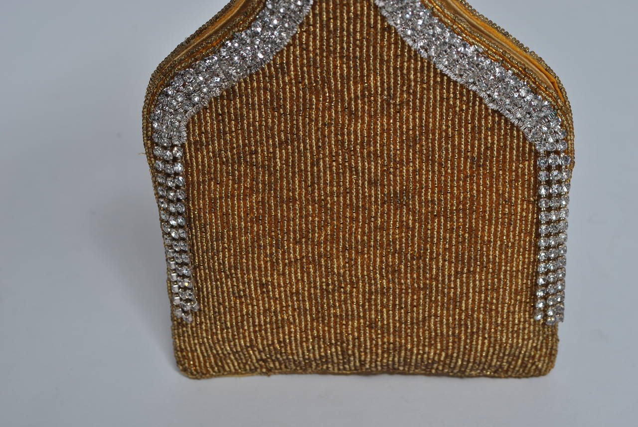 Unusual evening bag, produced in Japan mid twentieth century, one piece construction with integrated handle and composed of small gold beads outlined on edge with rhinestone strips and fringe. Lined in gold taffeta. Snap closure.