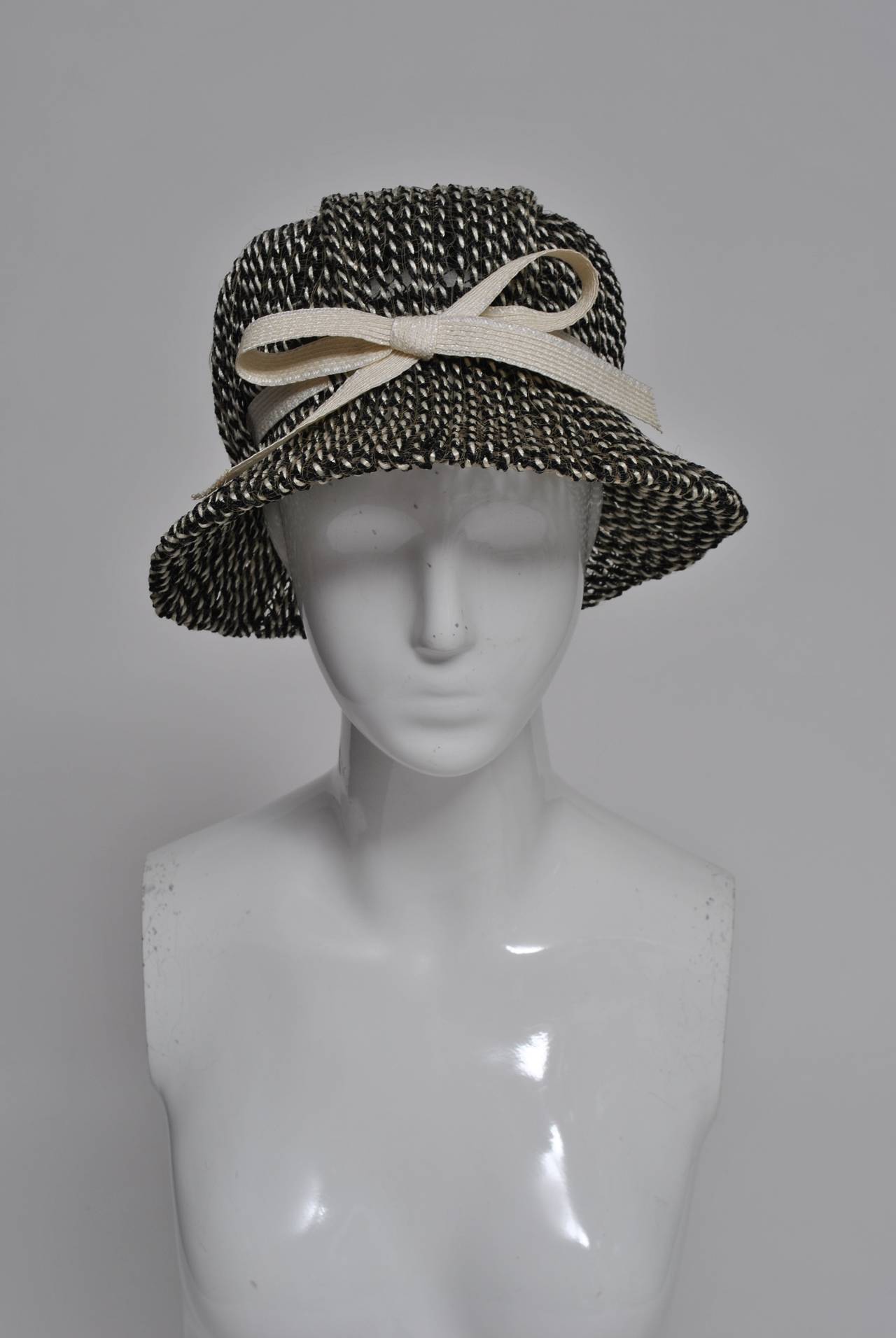 Unusual hat of twisted black/white straw on a mesh background featuring a wide brim and high crown. Beige ribbon trim with bow accents the hat. Looks unused. A beautiful example of the work of one of America's best milliners.