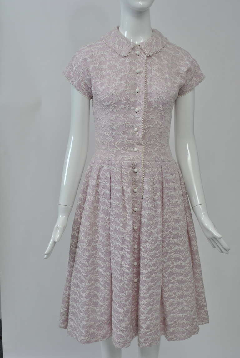 Lovely style and fabric in this summer dress of lavender voile embroidered allover with a repeat linear pattern in white and edged with a narrow white scallop. The shirt-style dress has an elongated, body hugging torso above a full skirt that starts