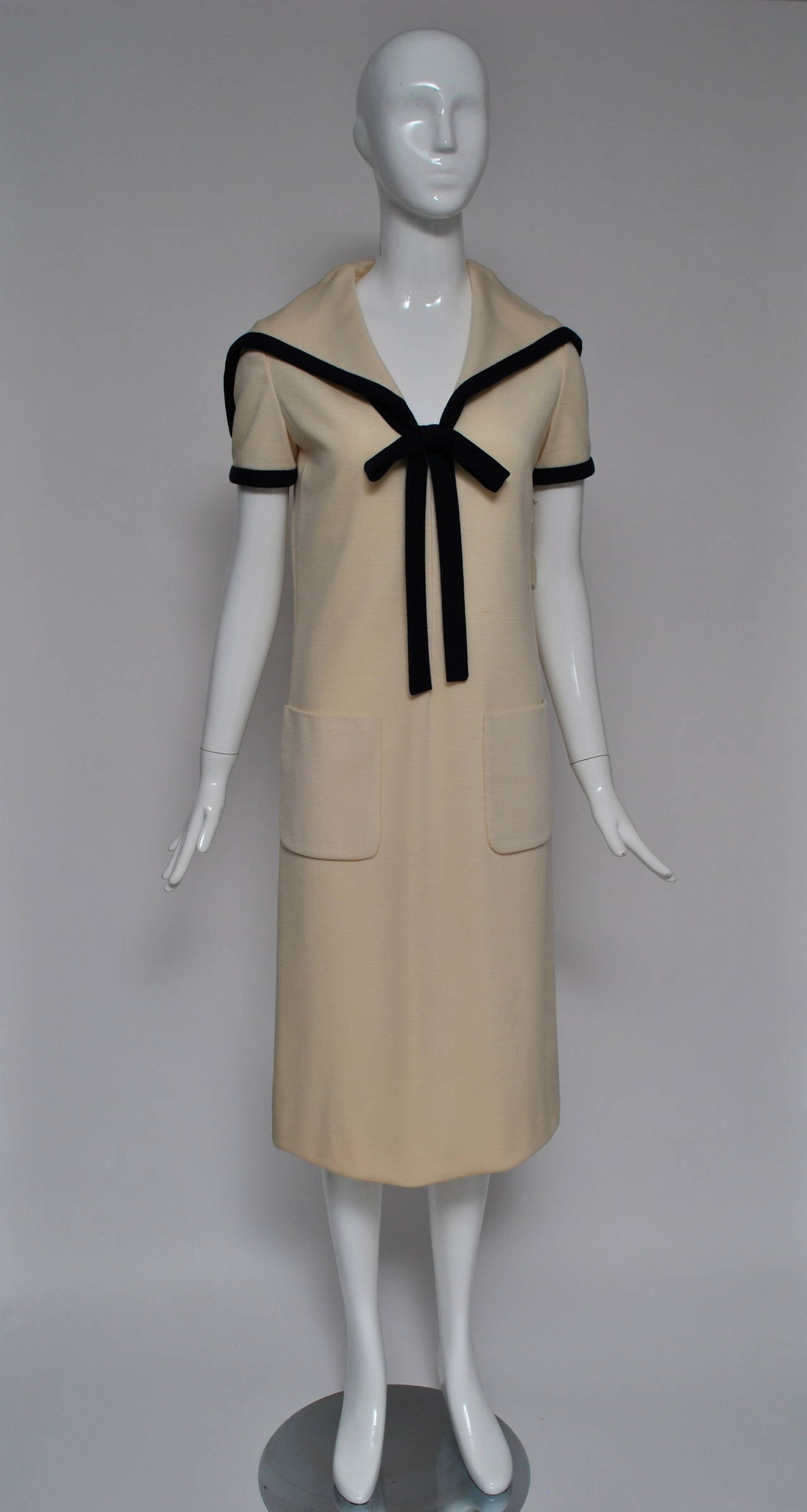 Bill Blass early 1970s sailor dress in white knit with square-back collar trimmed in navy, navy stars on back and navy tie with bow that hooks under collar. Front zipper. Patch pockets. Lined in silk.