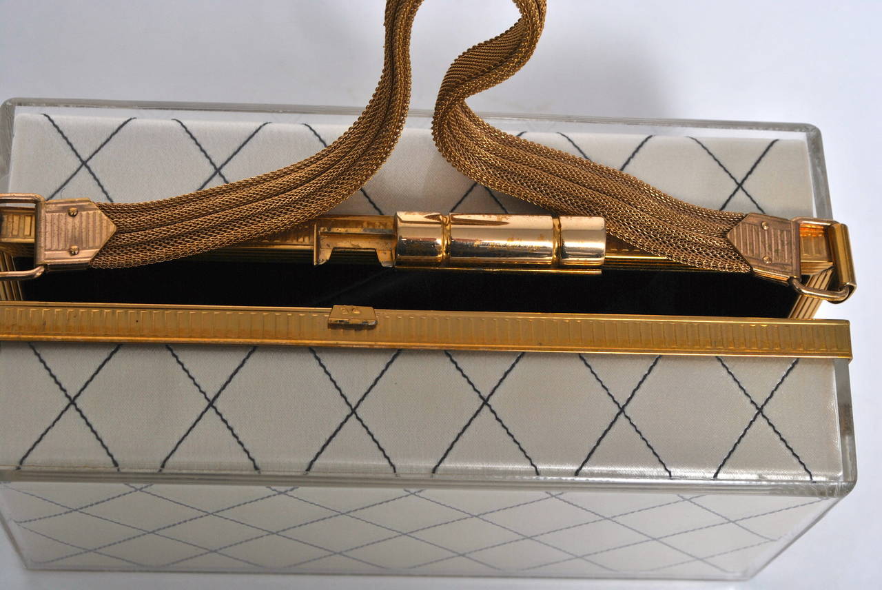 Unique rectangular box bag in clear lucite lined in off-white silk with a black stitched diamond pattern. Finished with interesting gold metal hardware and strap, typical of the fitted hard evening purses and compacts produced by Evans during the
