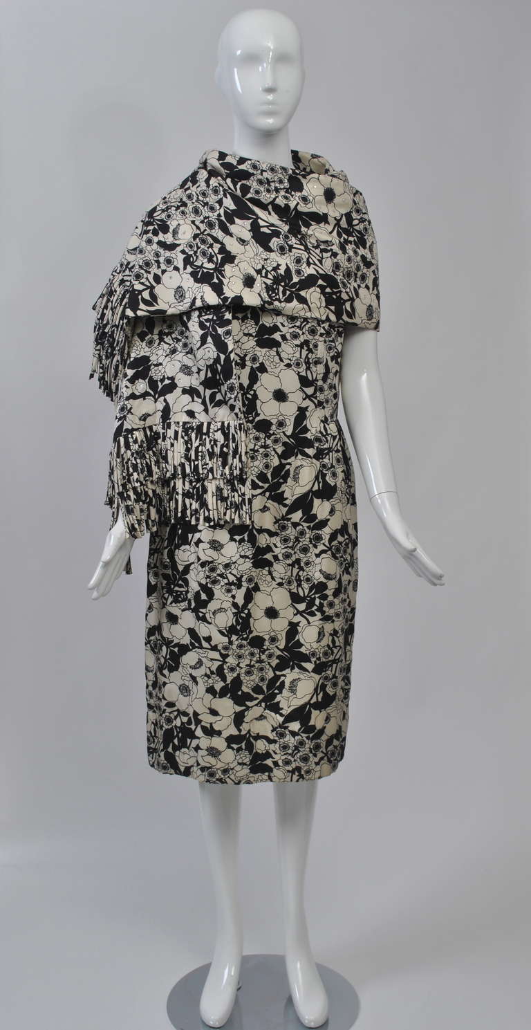 Classic style with a fluorish by Mr. Blackwell, this ensemble is fashioned of a black and white silk floral print. The sheath dress features a scoop neck, fitted bodice with ties at the armholes, and slim skirt that falls below the knee.