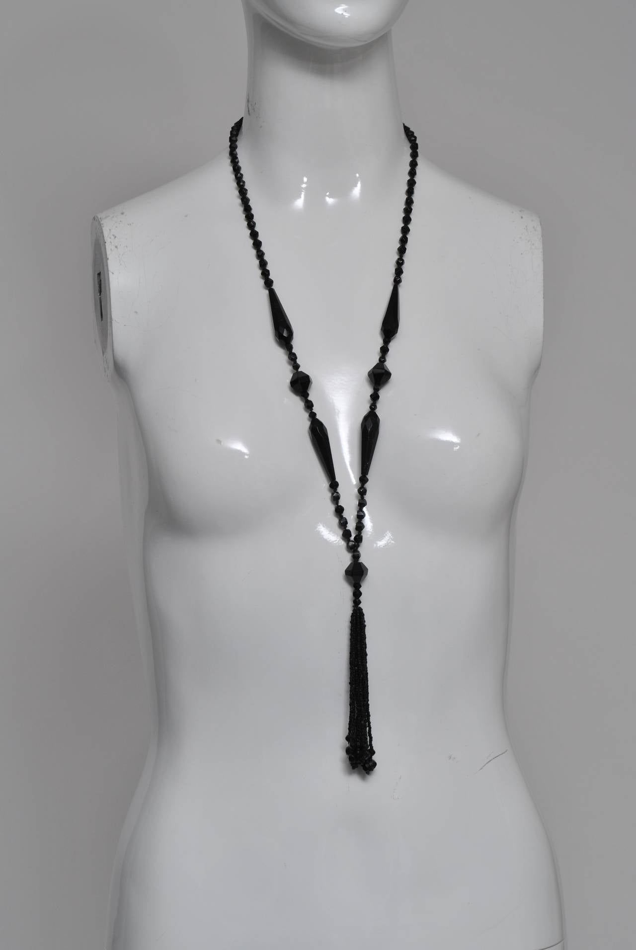 Long chain of small black cut glass beads interspersed with elongated and larger beads and terminating in a tassel composed of tiny beads. An elegant accompaniment to day or evening wear.