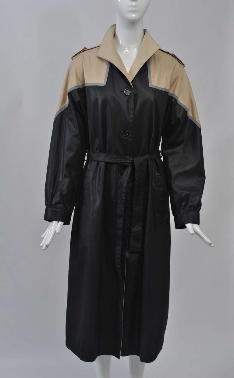 Bonnie Cashin black cotton raincoat from the 1980s with tan collar and yolk with epaulets. Style is single breasted with deep dolman sleeves and tie belt.
