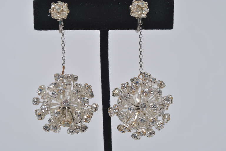 Rhinestone drop earrings with a space-age influence.  A sphere of multiple spikes terminating in small crystals is suspended on a narrow chain from a single ear stud. Screw-back closures.