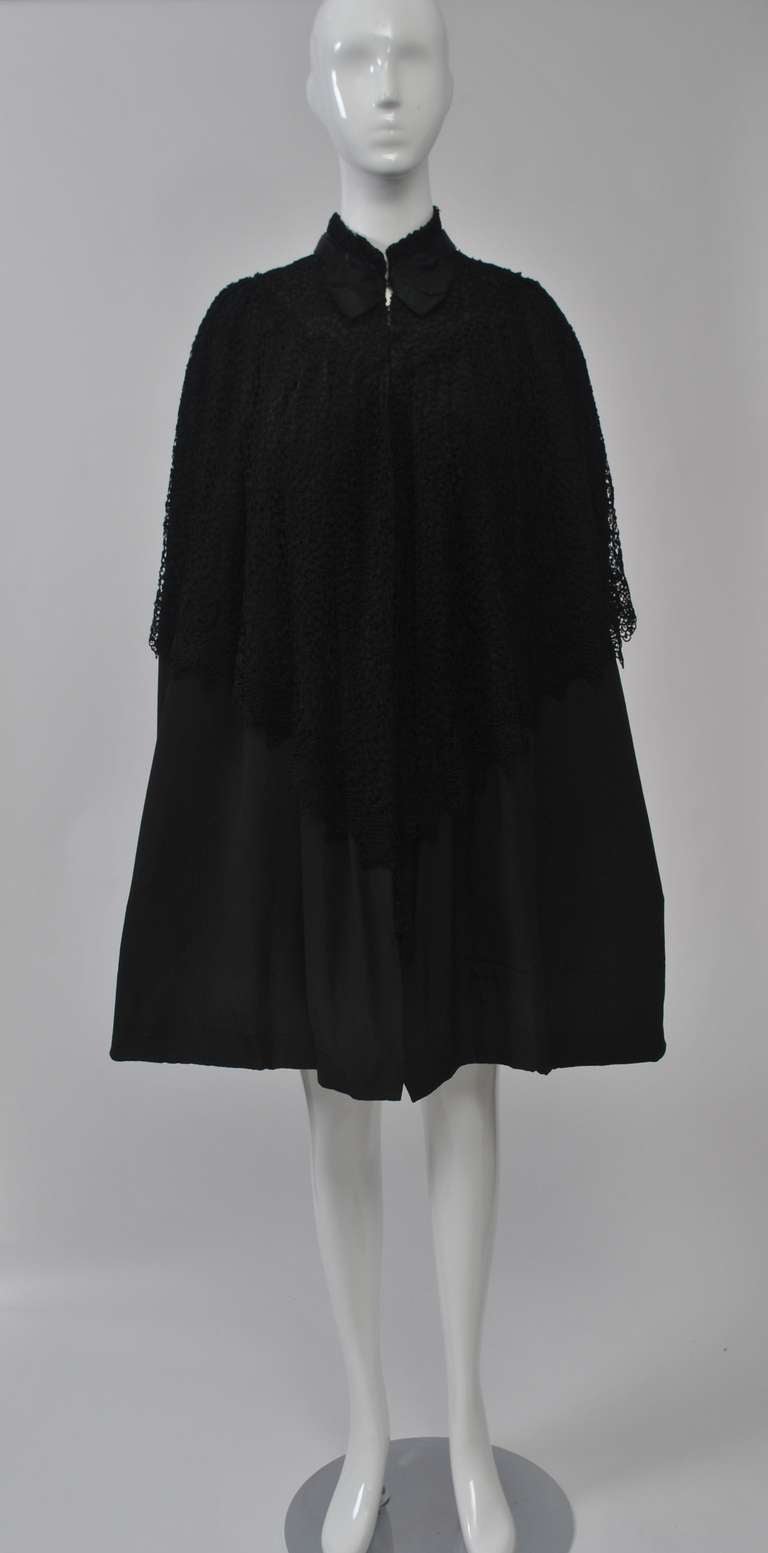 Early 20th-century black silk cape with an overlay of cotton lace at the mandarin collar and upper part. The lace has a border with pointed edging and dips to Vs front and back. A satin band and bow finishes the collar. Fully lined in silk. Parisian