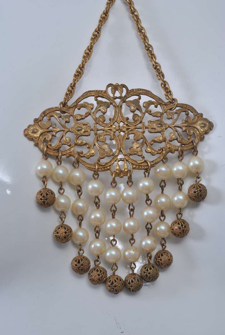Insolite collier vintage composé d'une chaîne accrochée à une perle au creux du cou avant de se prolonger vers le bas jusqu'à un médaillon percé suspendant perles et  des sphères percées. Belle patine.