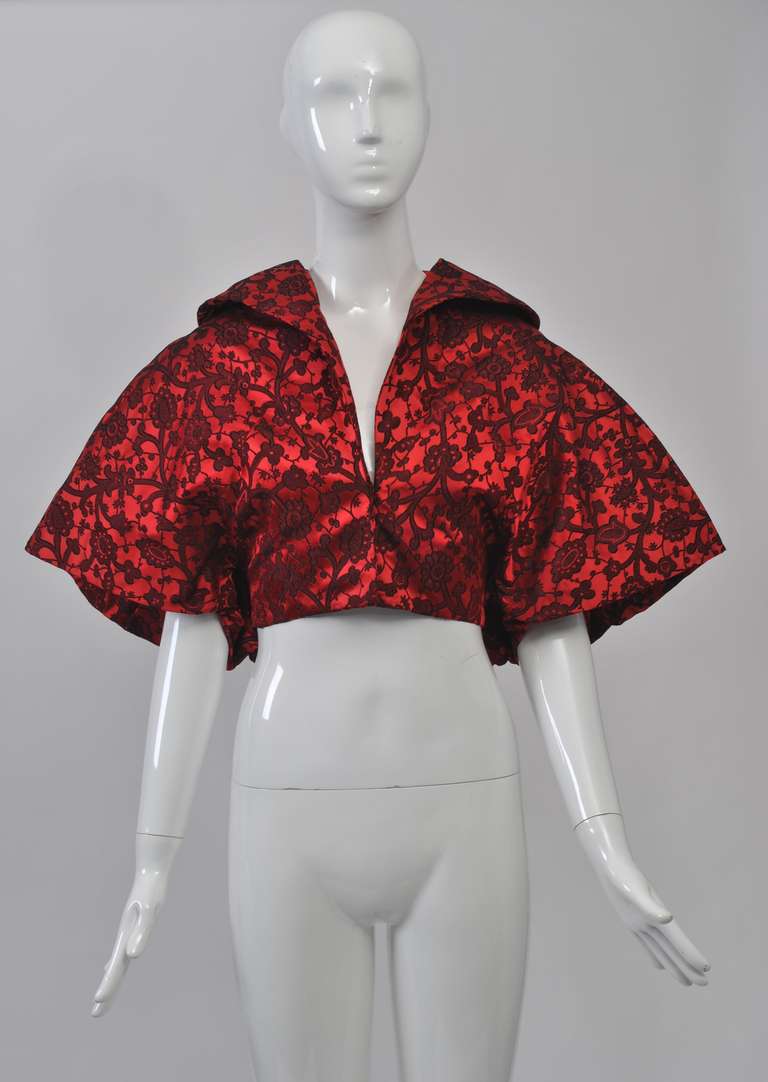 Fabulous styling on this beautifully detailed evening jacket fashioned of red and black brocade. The waist-length jacket is fitted in front and has butterfly sleeves that flow into the V-shaped balloon back. Underneath is intricate successive
