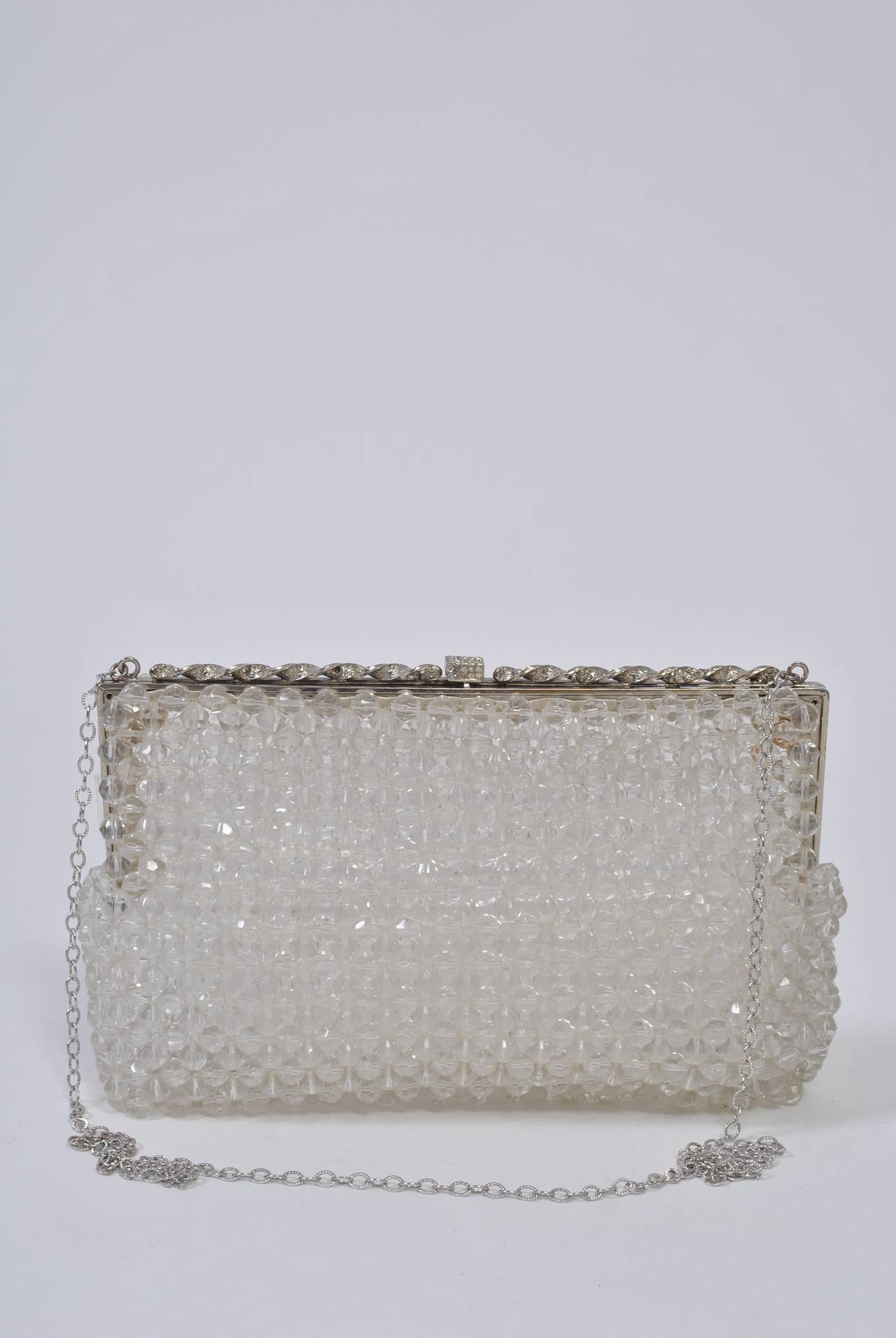 A fun shoulder bag of clear plastic beads aligned vertically and horizontally and having a silver metal frame with a rhinestone-studded twist motif and clasp at top. Long silver chain. Unlined but with satin borders on frame interior.