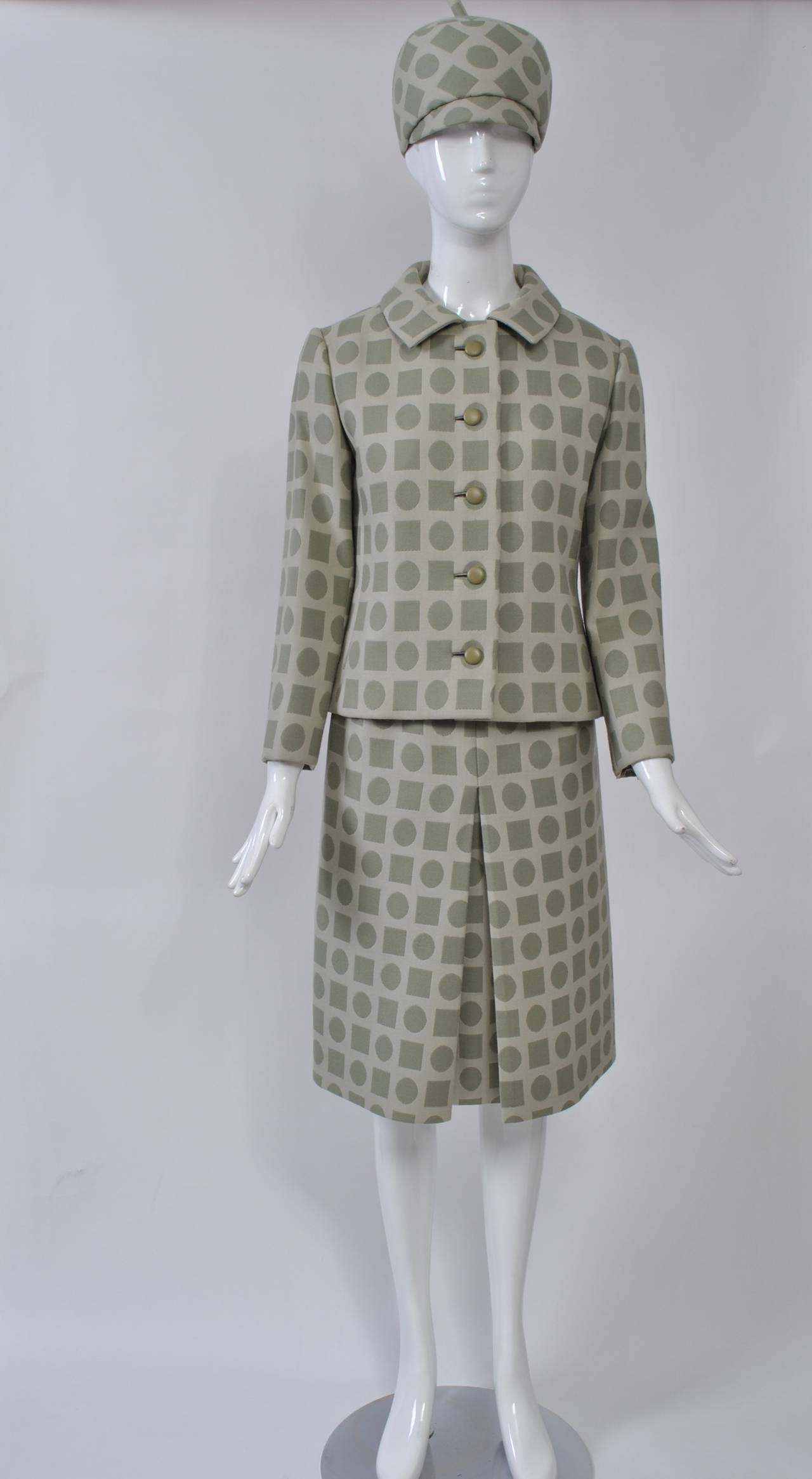 Bearing the Dior NY label, this fabulous suit and matching hat is fashioned of a jacquard wool in a subtle pale green yet bold geometric pattern of alternating circles and squares. The suit features a single-breasted, shaped hip-length jacket with a