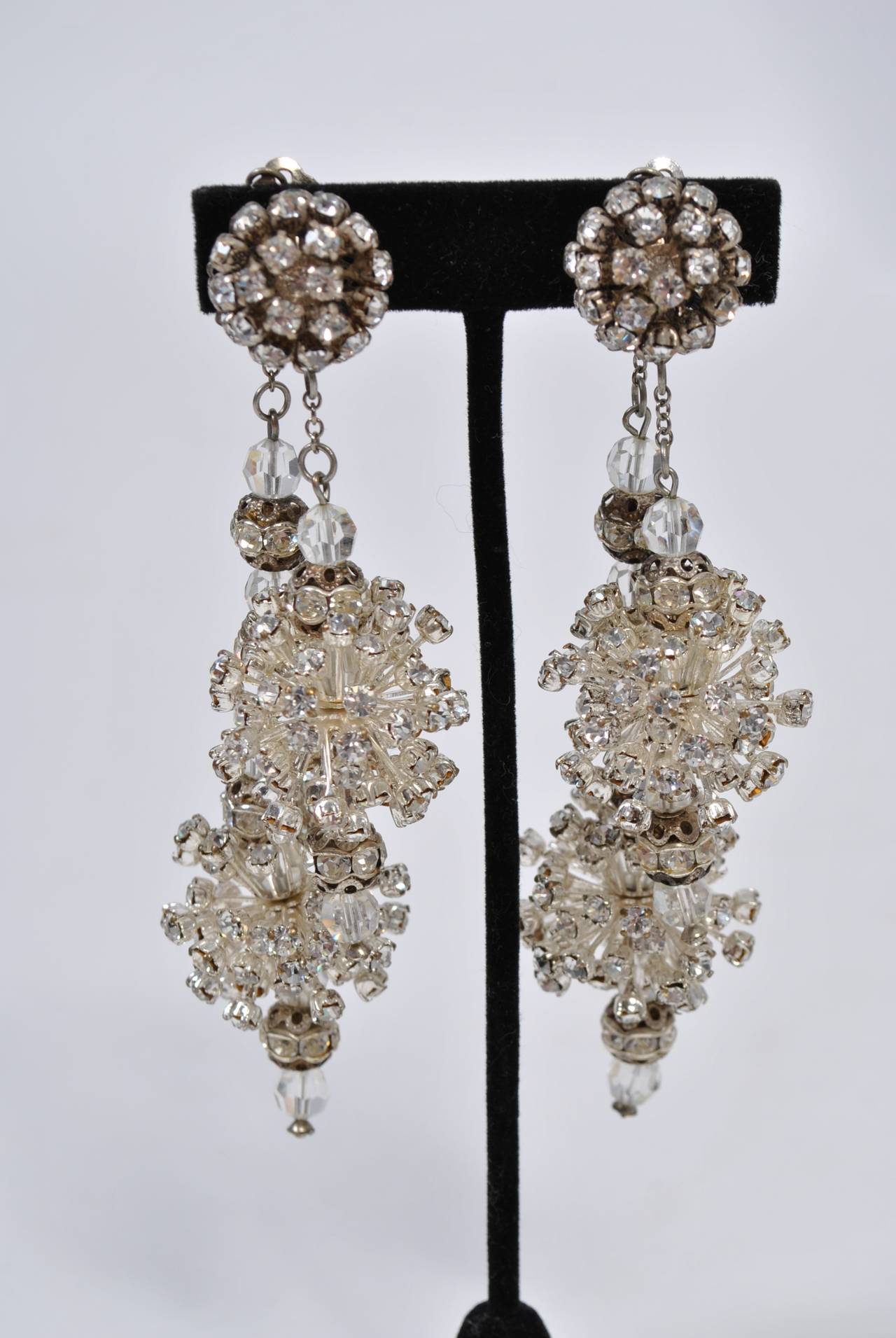 This striking pair of long rhinestone earrings will dramatize even the most simple  evening ensemble. At the earlobe is a round clip-on of small rhinestones that anchors two long drops, one that hangs in front of the ear and a longer one behind it.