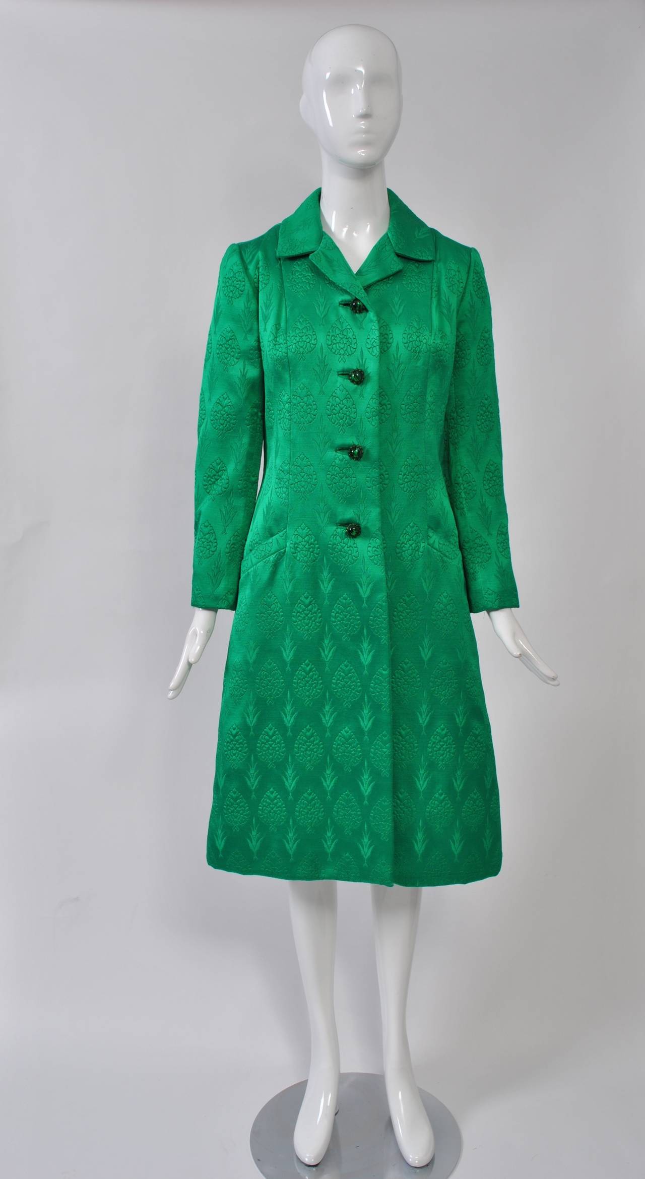 You will definitely get noticed in this bright green evening coat that is richly detailed with a repeating tree pattern. The single-breasted, A-line coat features bound buttonholes with matching stone buttons, slash pockets, a back belt, and back