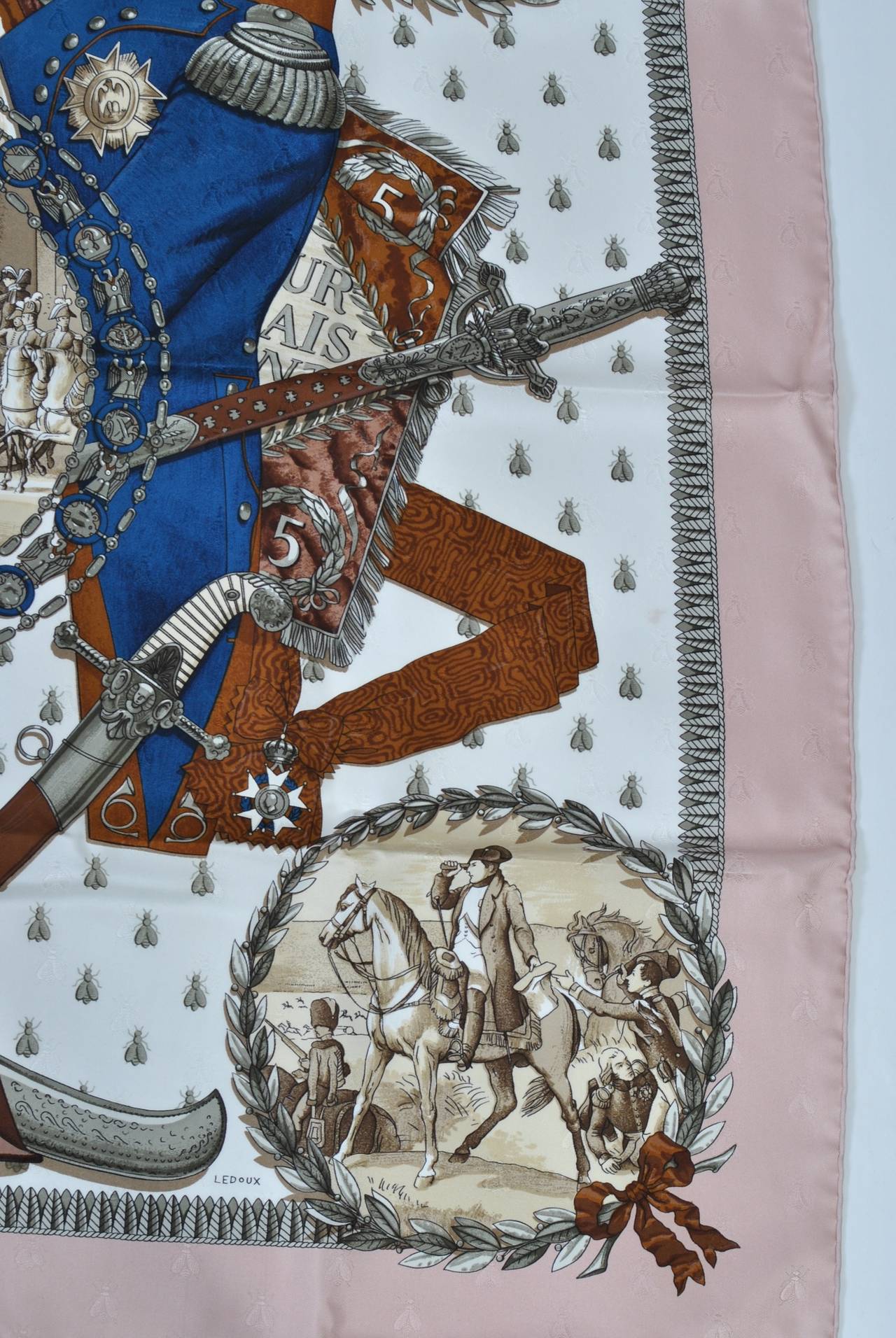 Hermès silk scarf commemorating Napoleon features a pale pink border and depicts scenes and items relevant to his reign. Hand rolled edges. Unused condition, in box. 1985 re-edition of a 1963 design by Ledoux. Measures 35