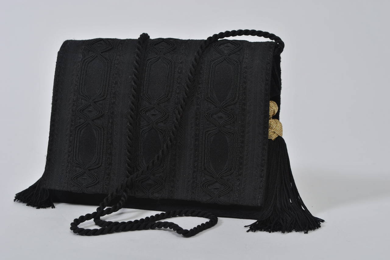 Convertible envelope clutch from Christian Dior Boutique fashioned of black suede body and passementerie satin exterior adorned with tassels and gold metal knots at each side. Optional black cord shoulder strap. Magnetic snap closure. Black satin
