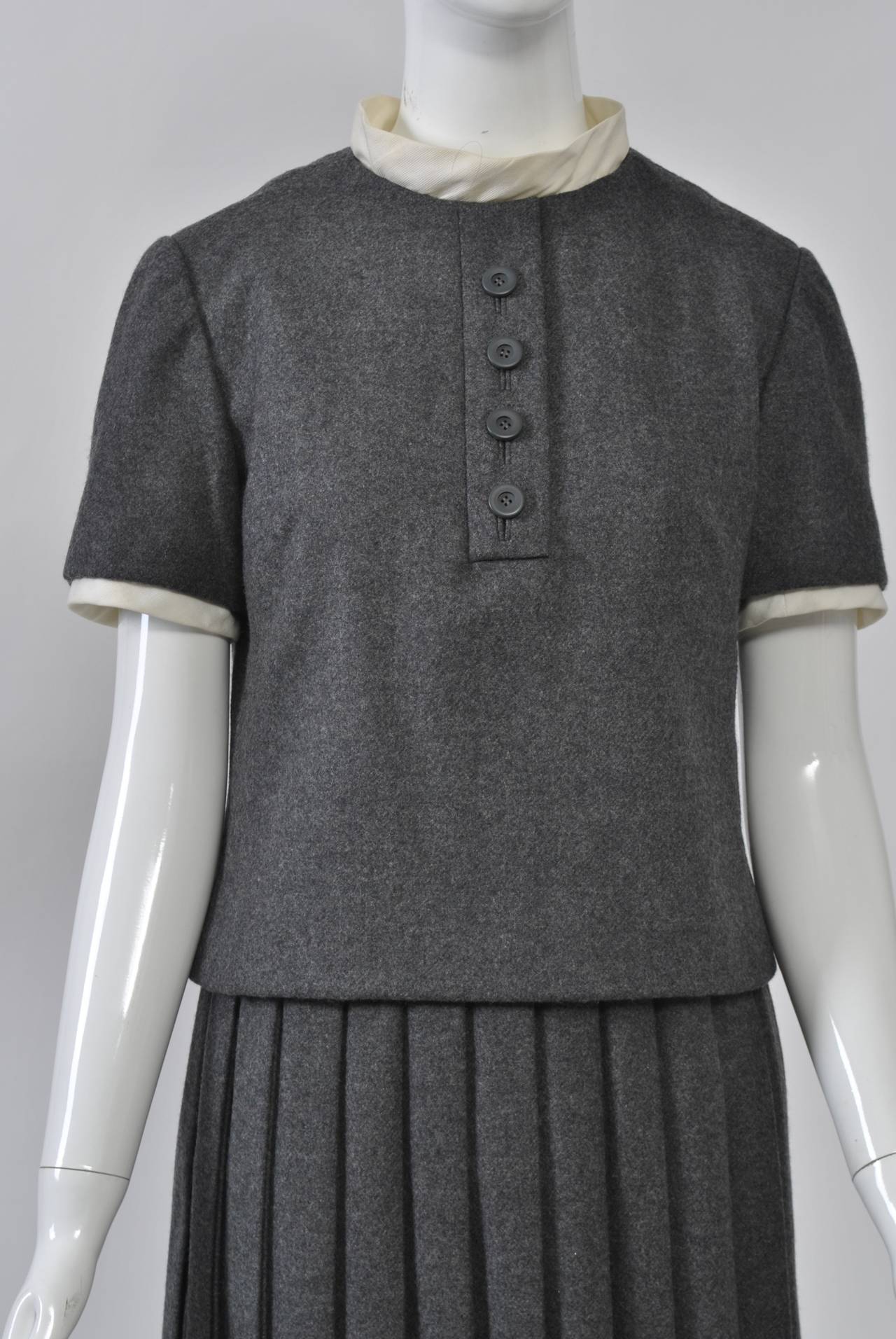 Christian Dior-New York c. 1960 two-piece dress in charcoal wool with white cotton detachable collar and cuff attachments. The short-sleeve, hip-length overtop has a tab and four buttons down the front and a back zipper. the skirt has double-knife