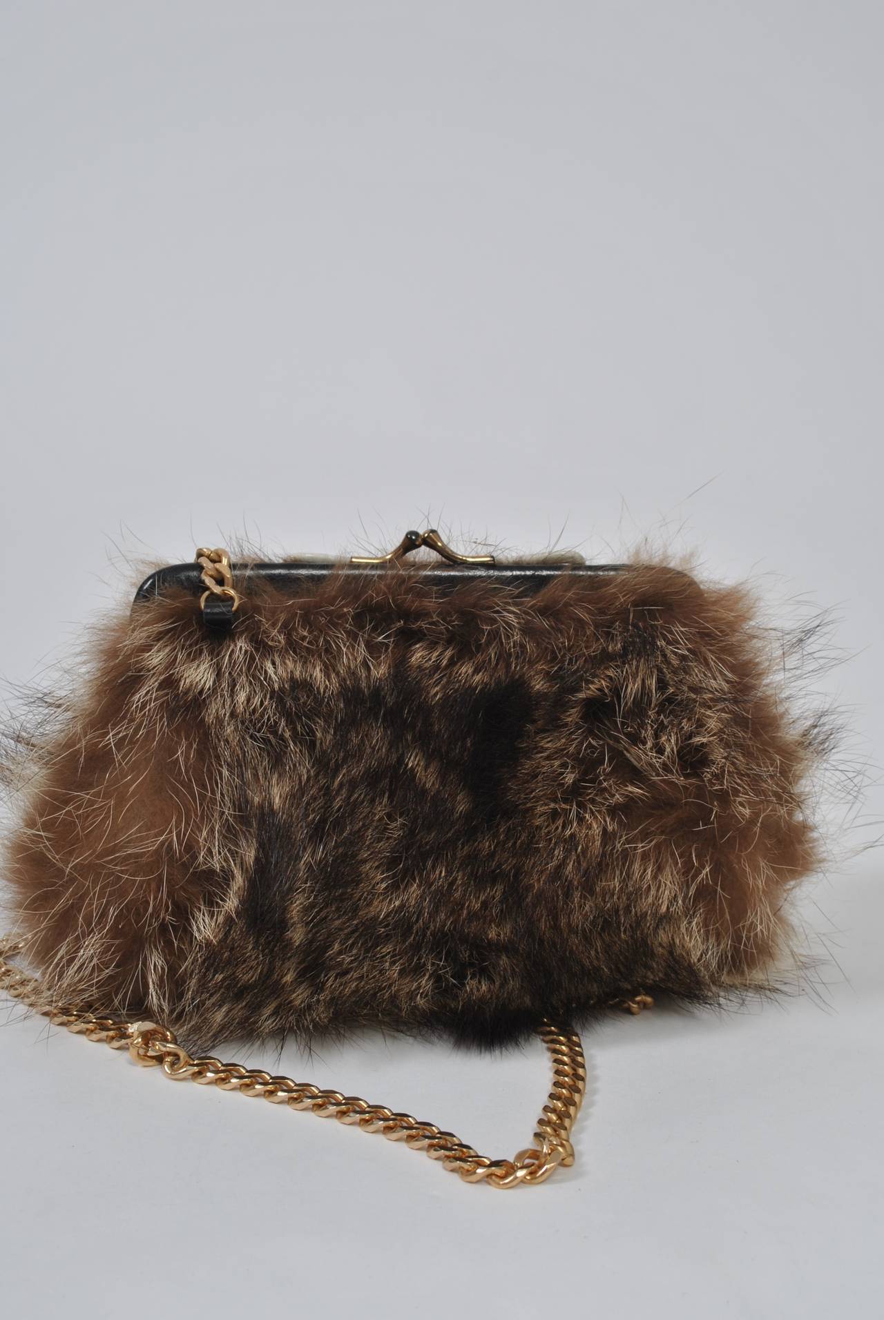 Small shoulder bag in fur, probably raccoon, with black leather frame and long gold chain. Black interior. Unmarked. Chain length: 37