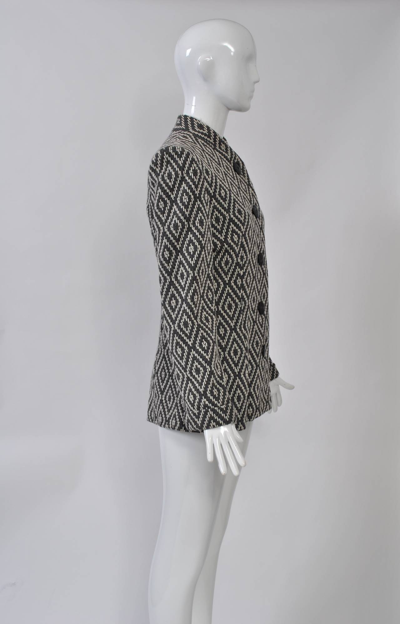 Trigère's clothing was always simply elegant and tailored well. This jacket is no exception. Fashioned of gray and ivory knit in a diamond pattern, it features a collarless, funnel neckline, single-breasted and slightly shaped styling, and narrow