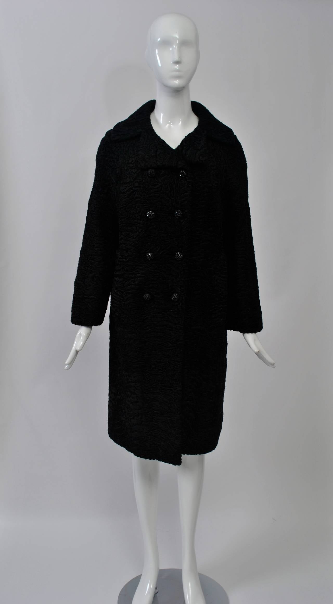 A classic, double-breasted coat in black Persian lamb, the fur tightly curled and compact. Dressy buttons are dome-shaped studded with black rhinestones. Side pockets.  Silk lining. All in excellent condition. Approximate size 6-10. Timeless styling