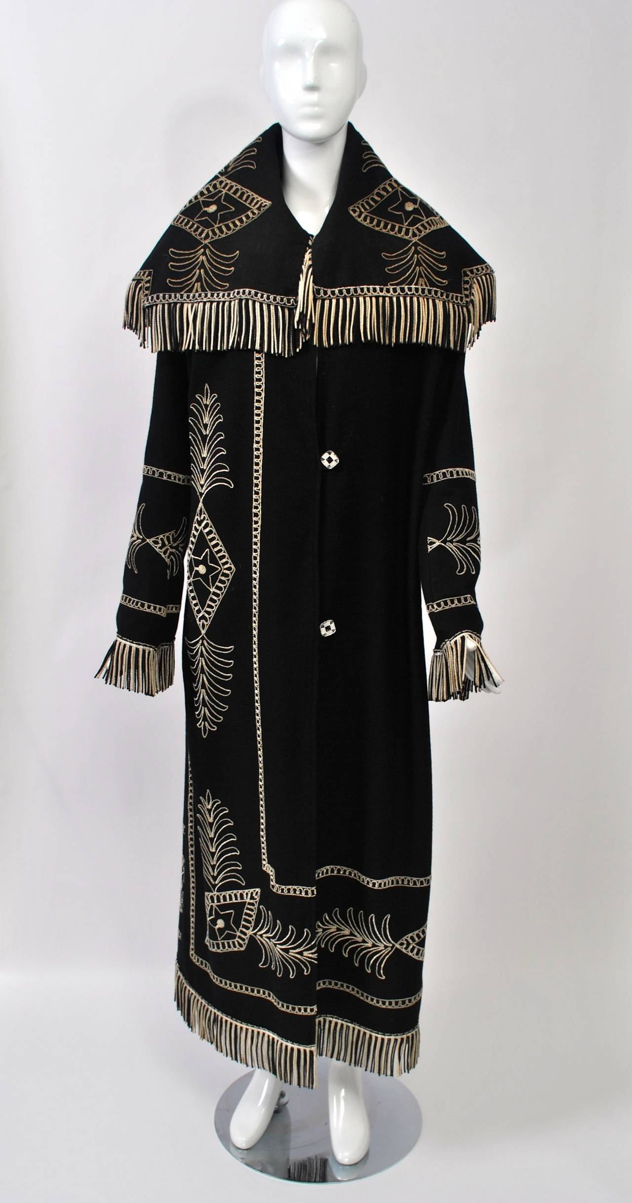 Extraoridinary and unique coat in a fine black wool enlivened by beige embroidery and trimmed with beige and black fringe. Purportedly partially fashioned from French 1890s portieres in 2006, the long coat has a huge stand-up collar and three