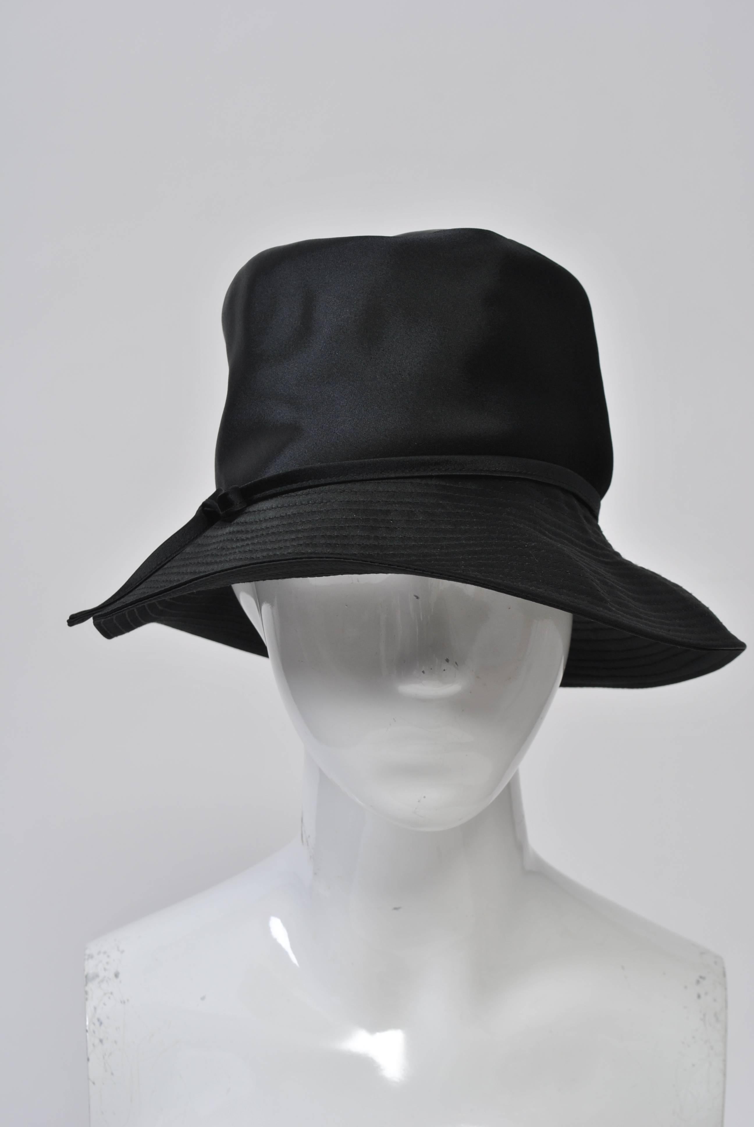 Black satin hat with narrow band and side bow, stitched brim. Made by Betmar, retailed by Bonwit Teller. Looks unworn. Medium size.