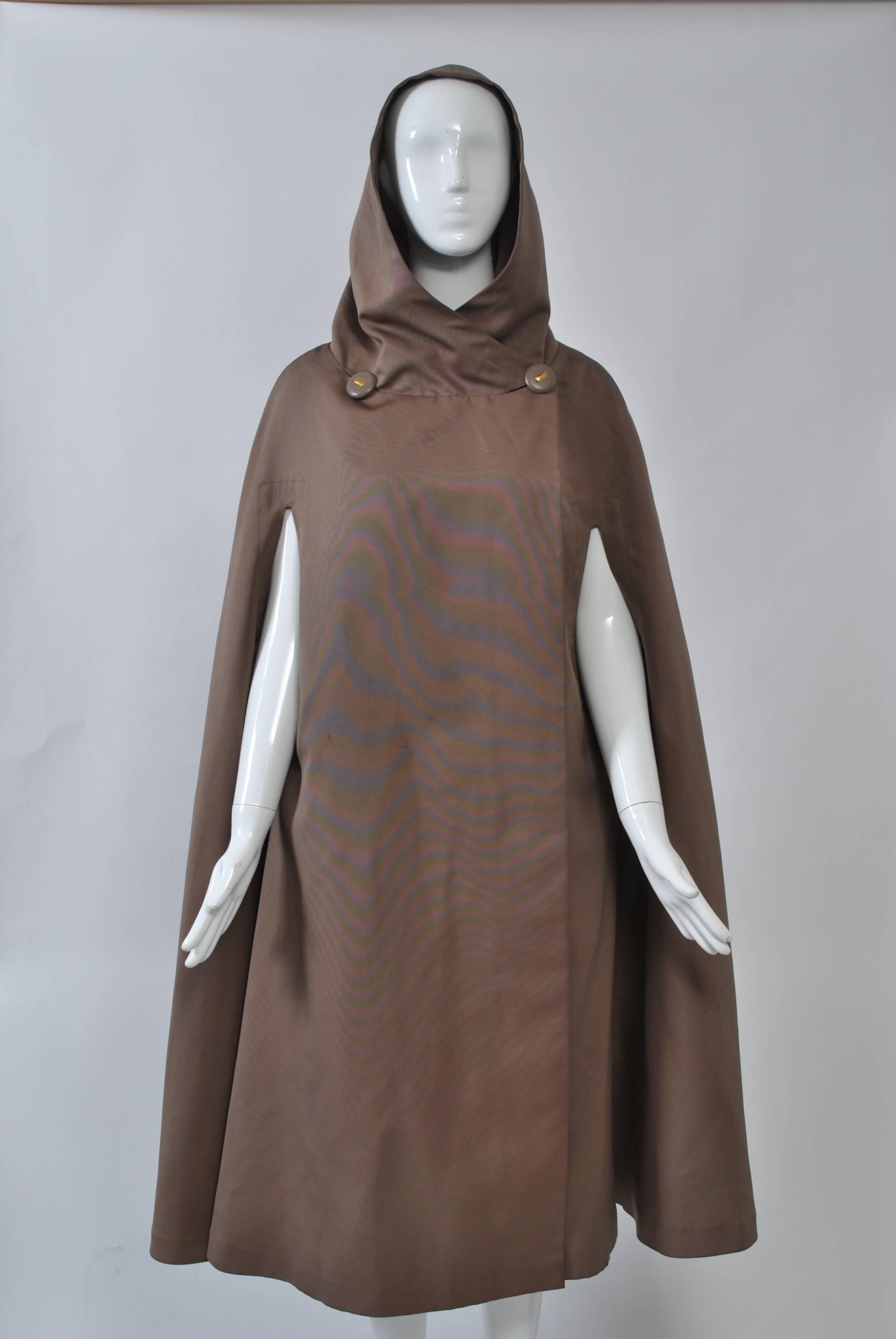 Full-length cape by Pauline Trigére in cocoa silk faille with hood that forms stand-up collar when down. Arm slits, overlap secured by two buttons at neckline, the buttonholes concealed in the neck seam. Unlined.