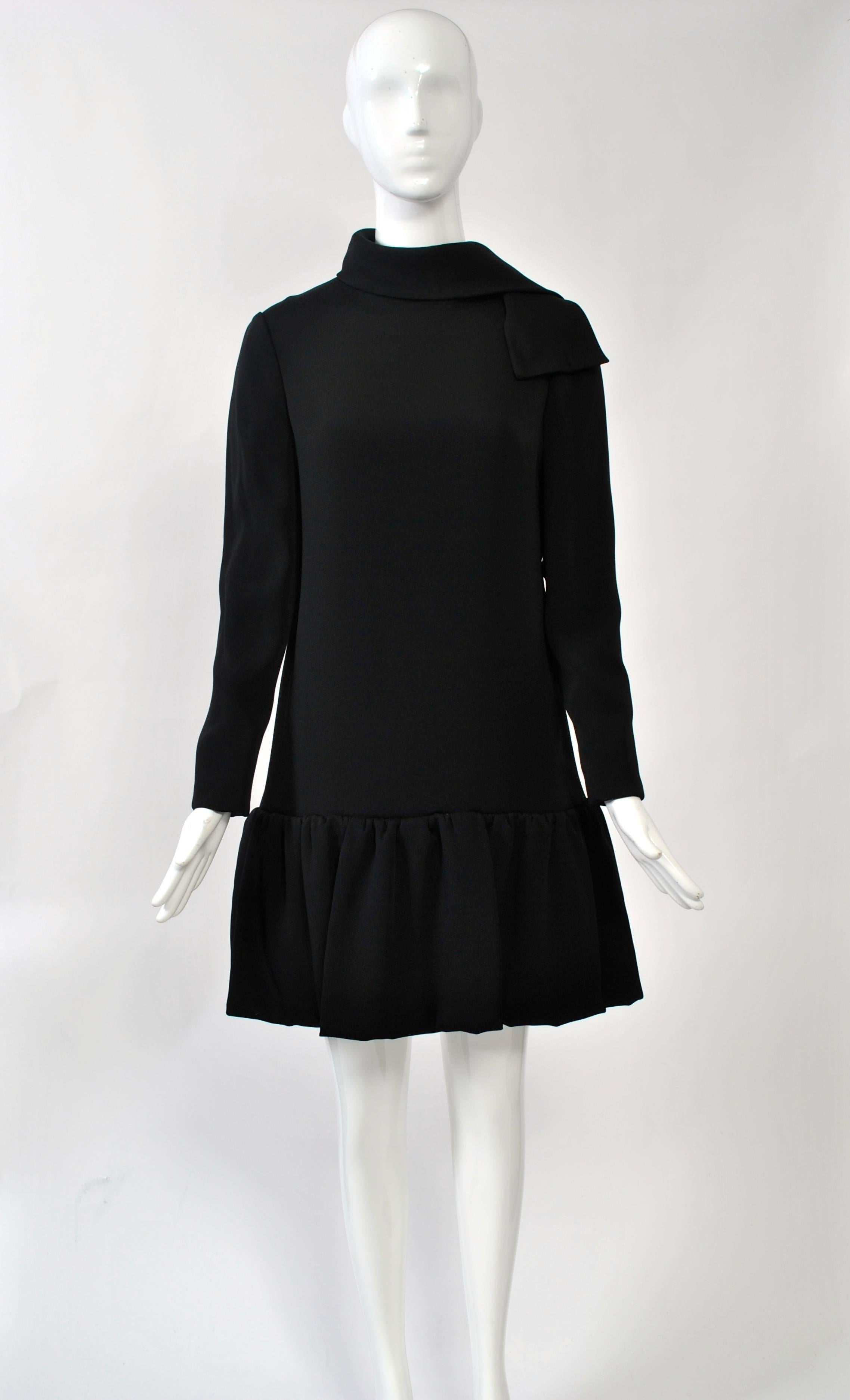 1960s Pierre Cardin LBD in heavy black crepe featuring a narrow silhouette with dropped waist and a uniquely designed skirt made of looped and shirred panels. Long sleeves and a long neck tie complete the look. Back zipper. Fully lined. Approximate