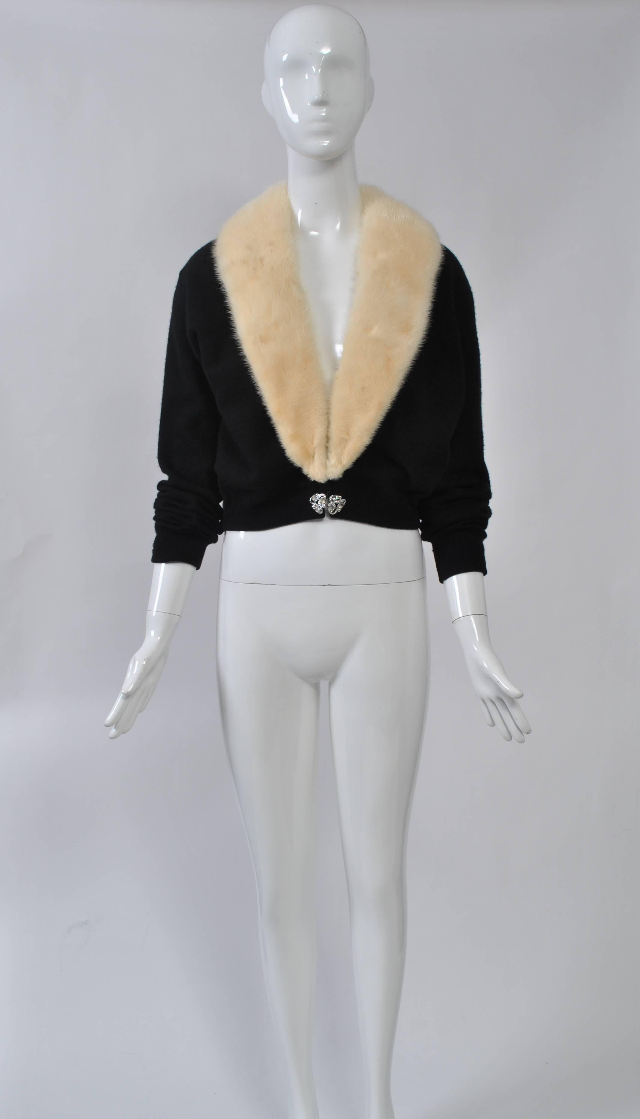 Black cashmere cardigan with detachable white mink collar. Rhinestone clasp at waist, rhinestone buttons at wrist. Collar attaches to sweater with snapped tape and can be removed for cleaning the sweater. Sheer lining with lace.