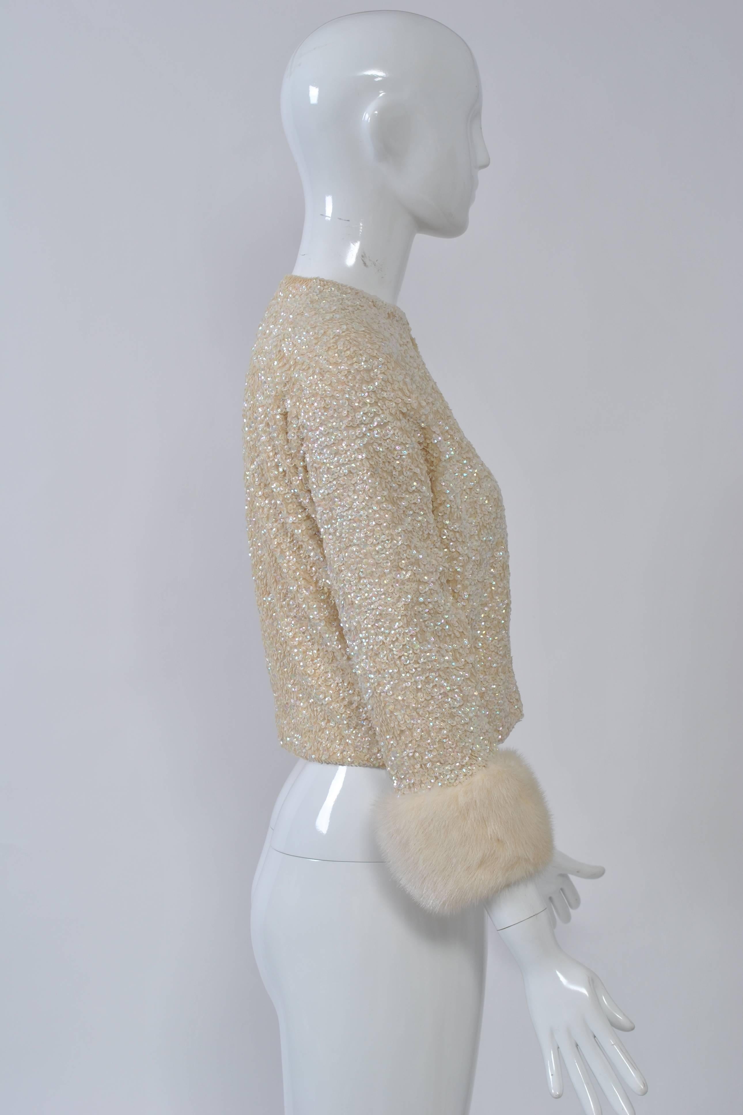 Off-white wool cardigan covered with iridescent sequins and with three-quarter sleeves trimmed in white mink. Waist-length, collarless with hook-and-eye closures down front. Lined in silk.